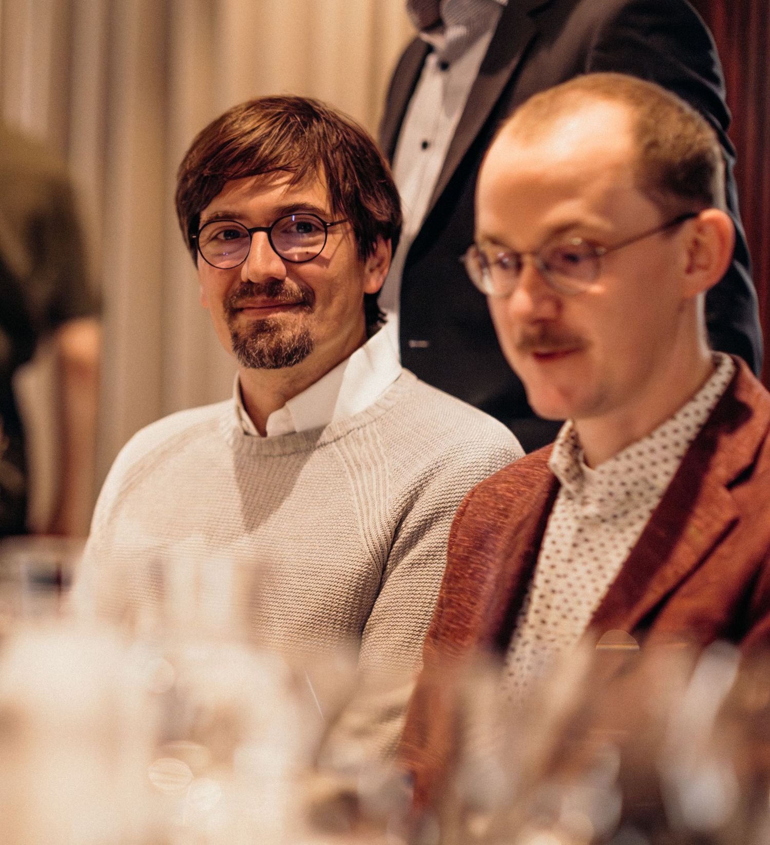 A group of people in glasses and casual attire sit together at a table in warm lighting.