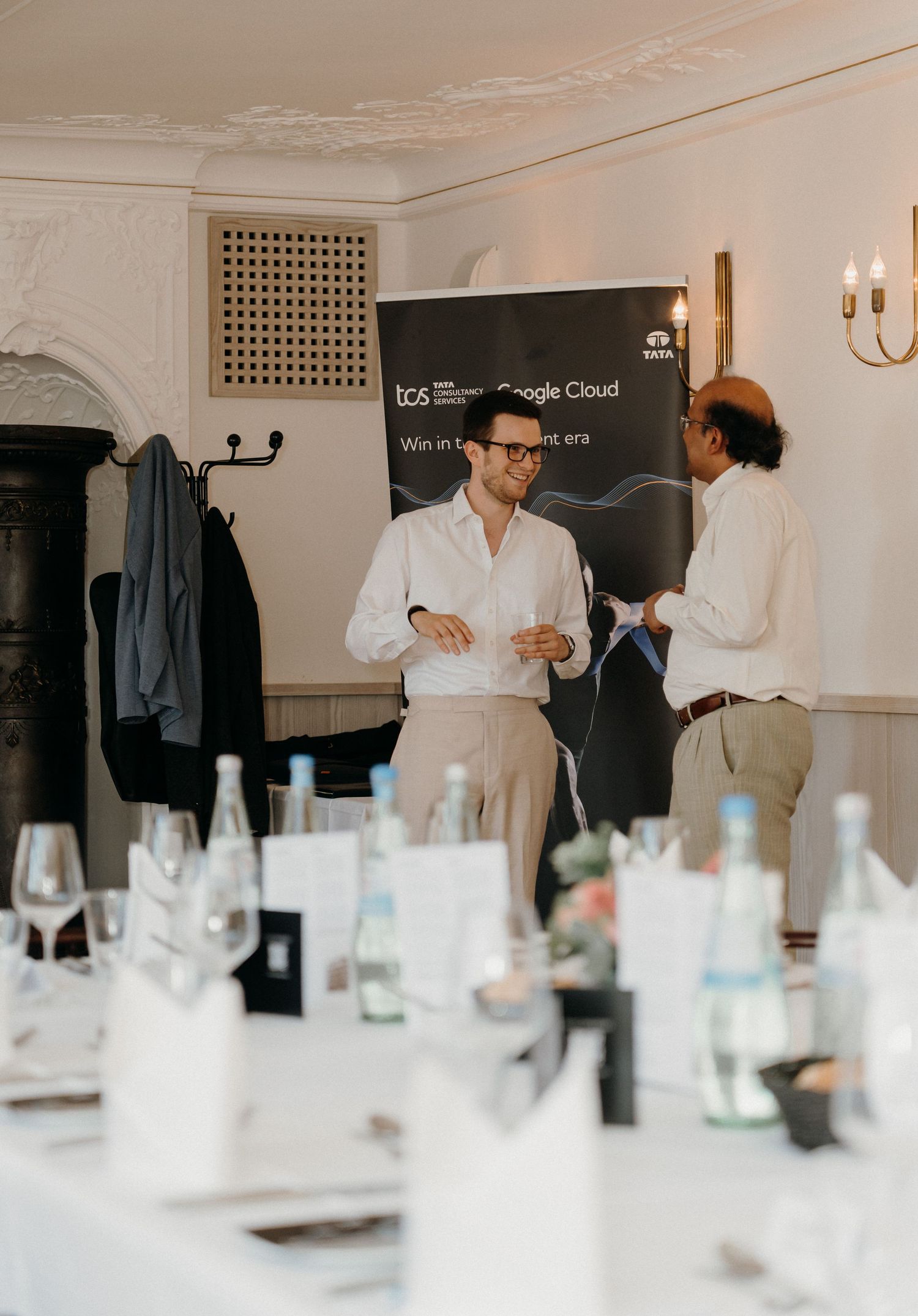 Two professionals networking at a TCS Google Cloud event, standing near a branded banner in an elegant dining room.