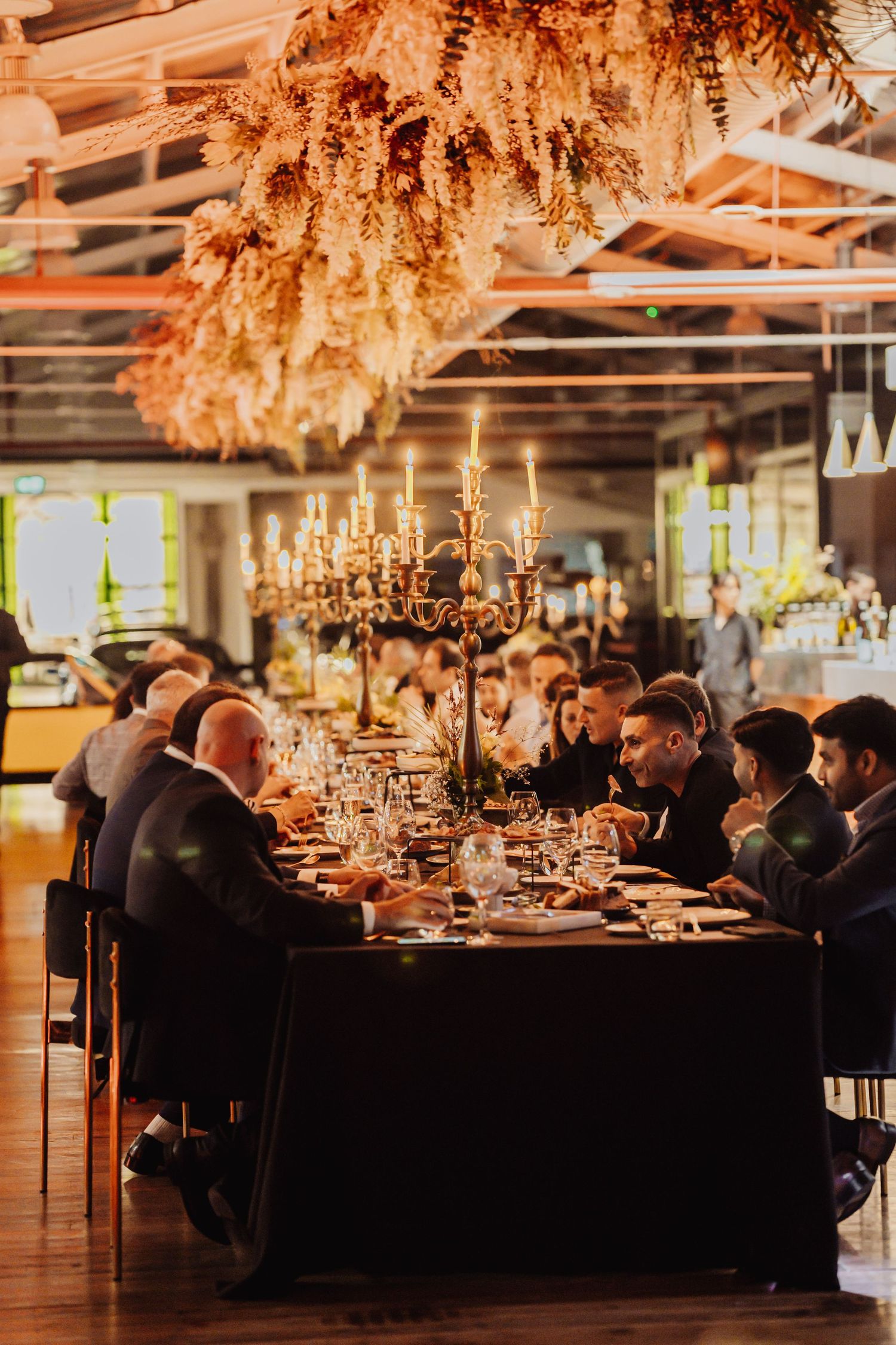 Elegant wedding reception dinner setup with long tables, candelabras, and dried floral arrangements in a rustic venue.