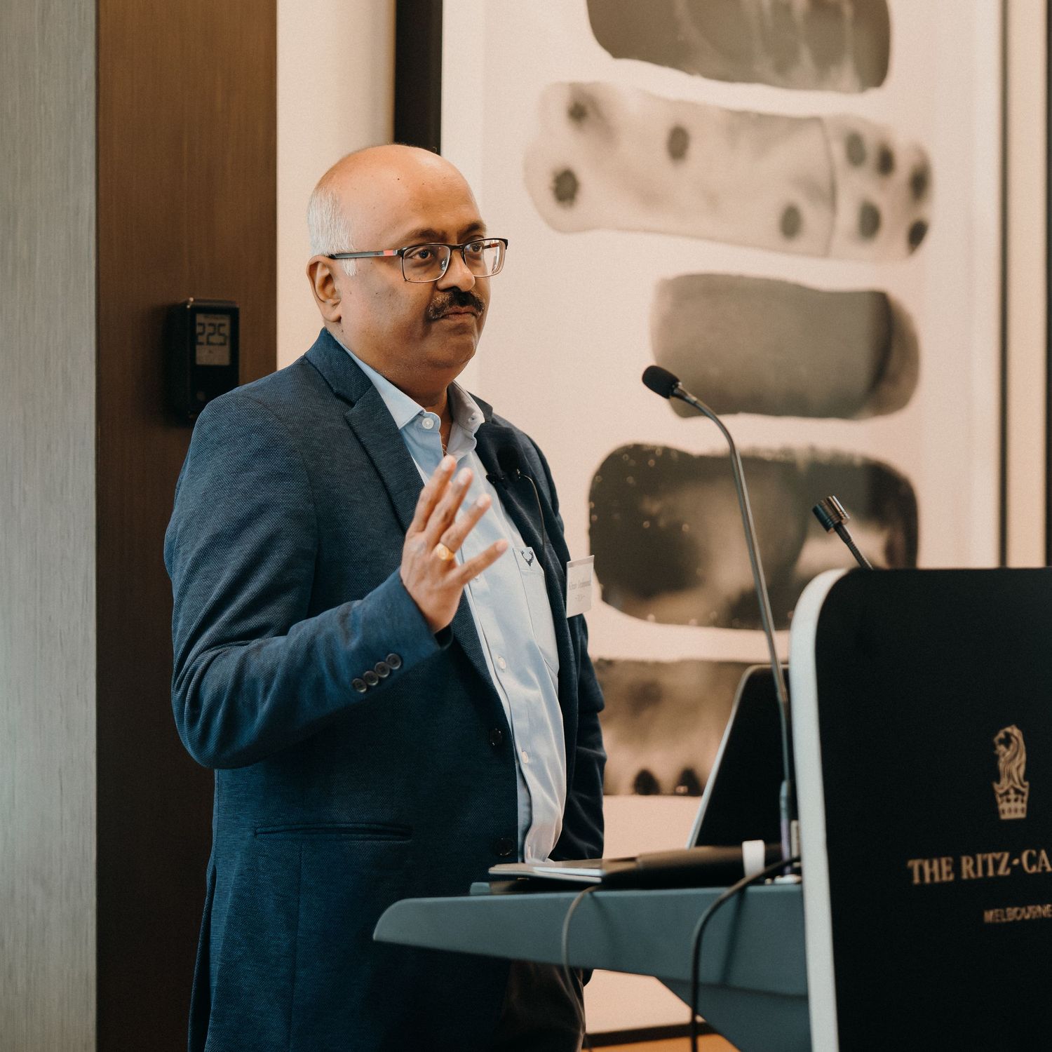 A speaker gives a professional presentation while standing and gesturing in an office meeting room.