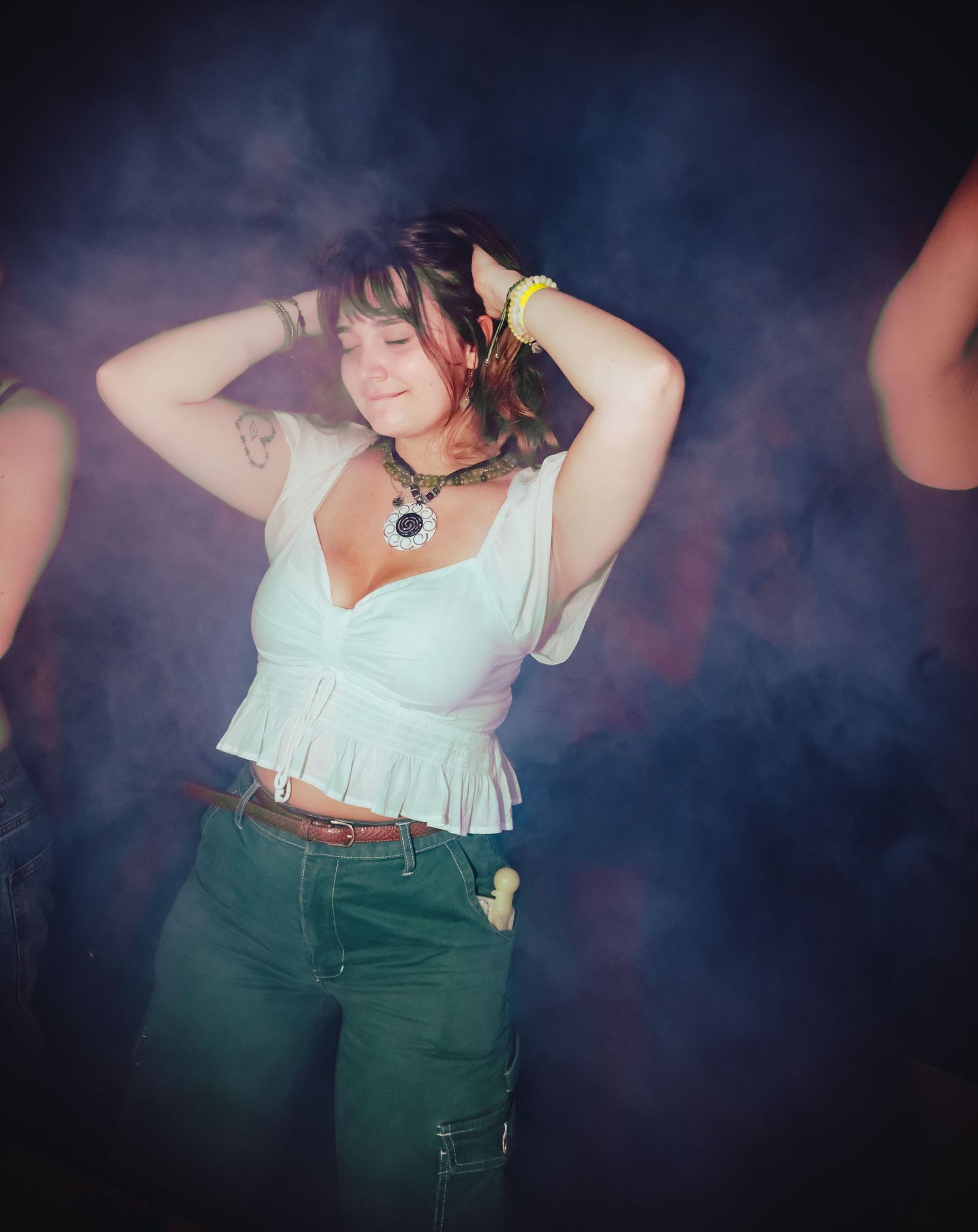 A retro-styled photoshoot featuring a white blouse and green high-waisted pants against a smoky dark background.