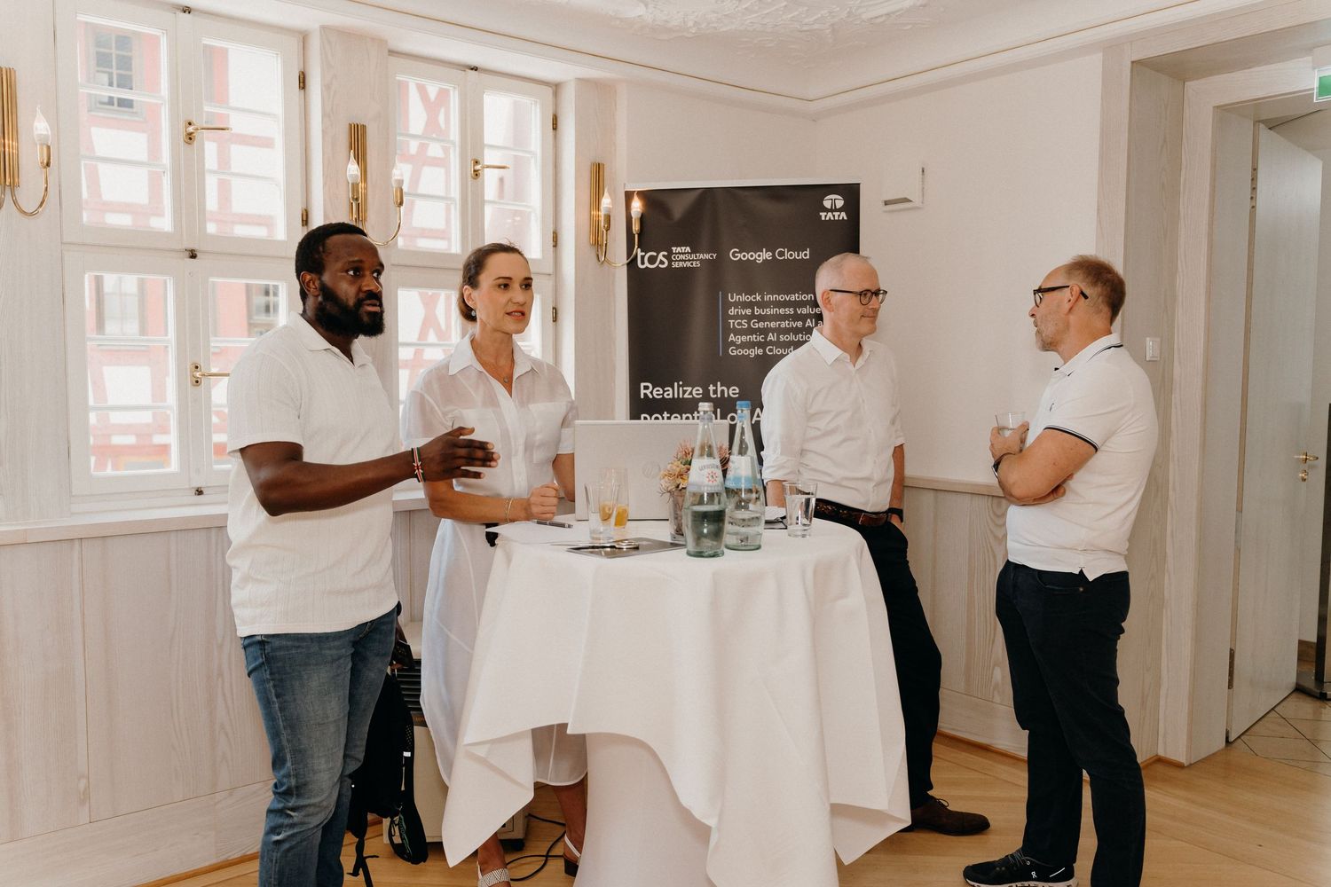 Four professionals networking at a business event, standing around a high table in an elegant white room.