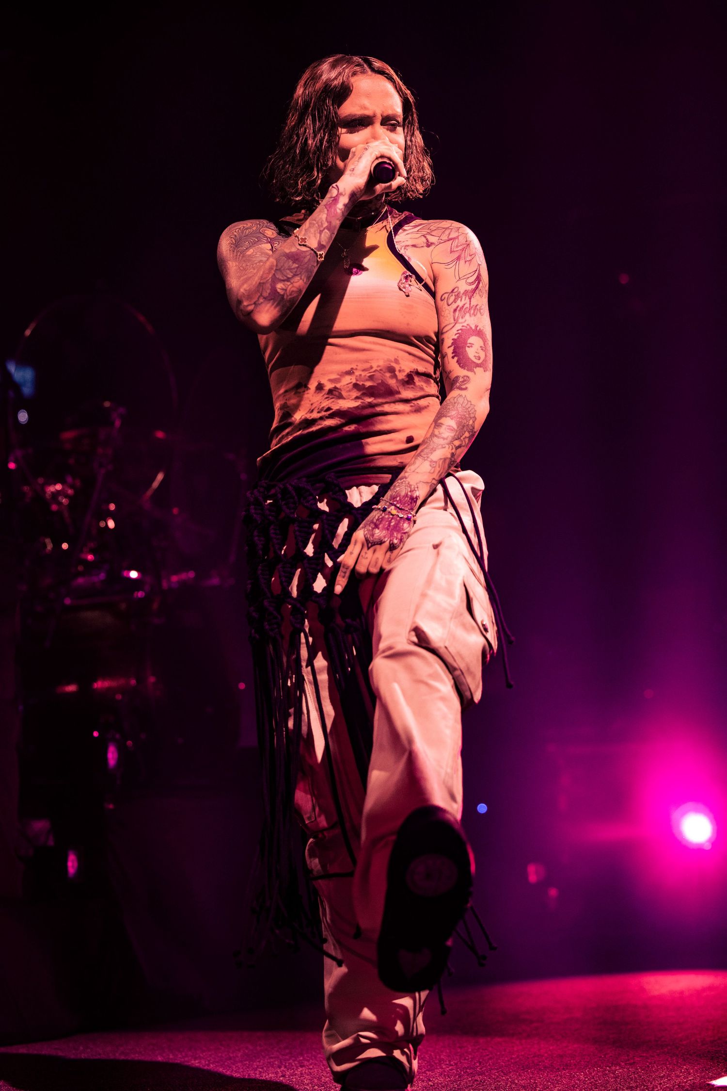 Performer in white clothing silhouetted against purple stage lighting during dramatic concert performance.