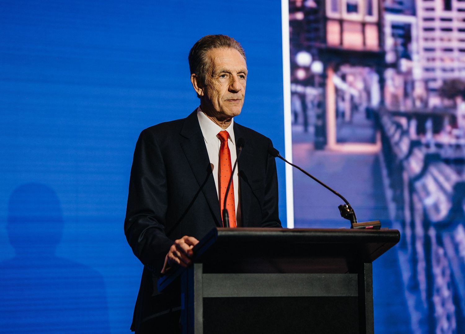 A speaker stands at a podium against a blue backdrop during a presentation event.