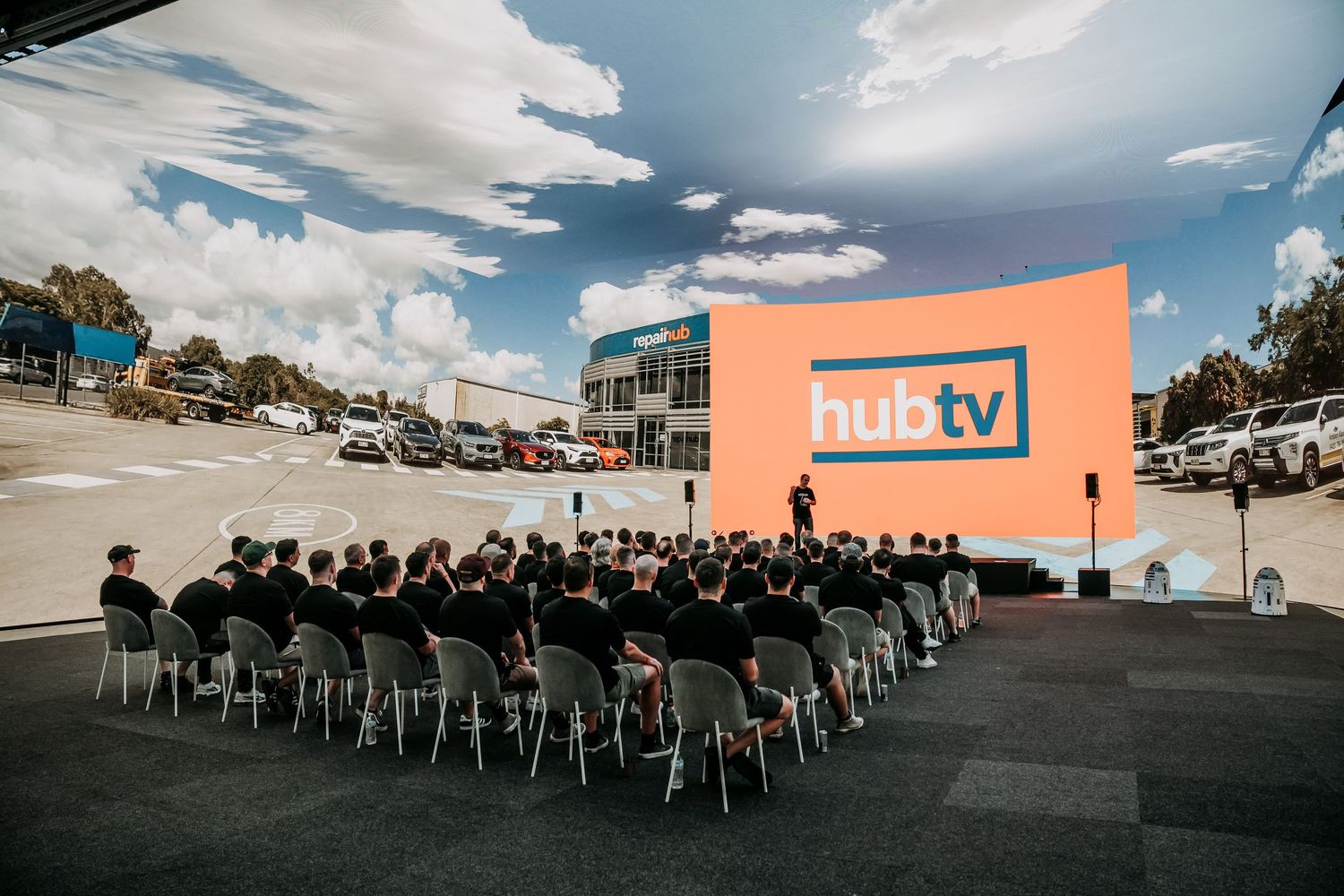 Outdoor drive-in movie theater setup with rows of empty chairs facing a large screen at dusk.