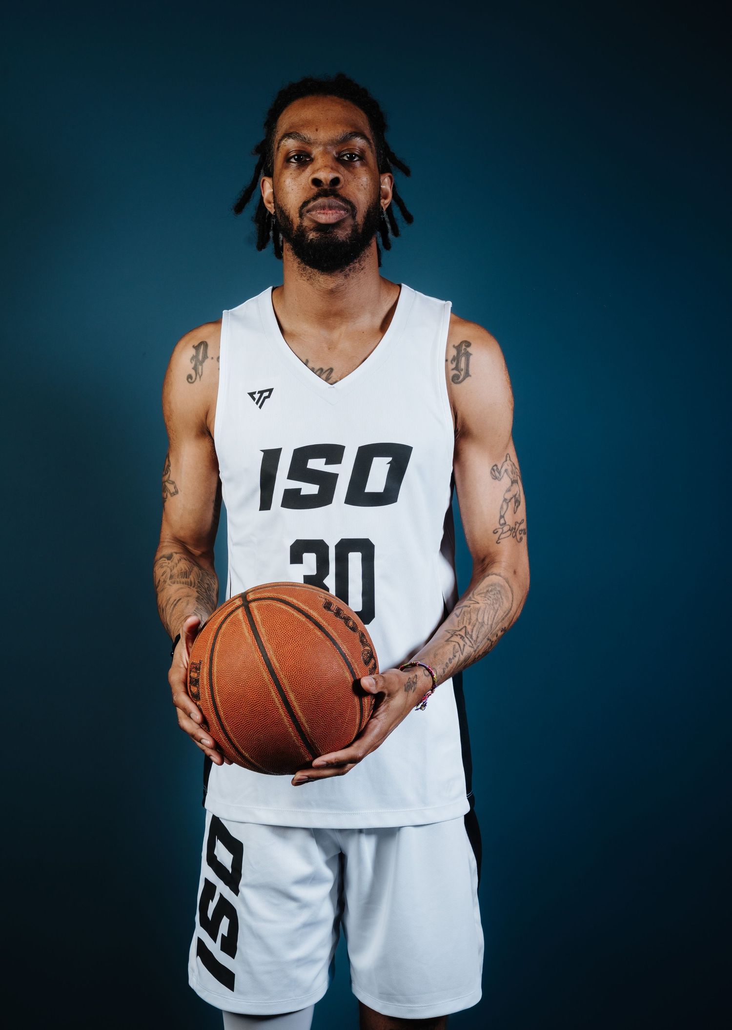Basketball player in white jersey holds ball against dark background in professional sports photoshoot.