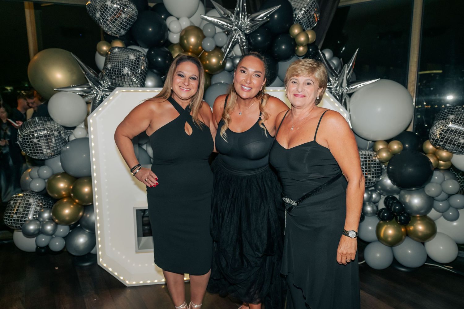 Friends posing together at a party with silver and gold balloon decorations in the background.