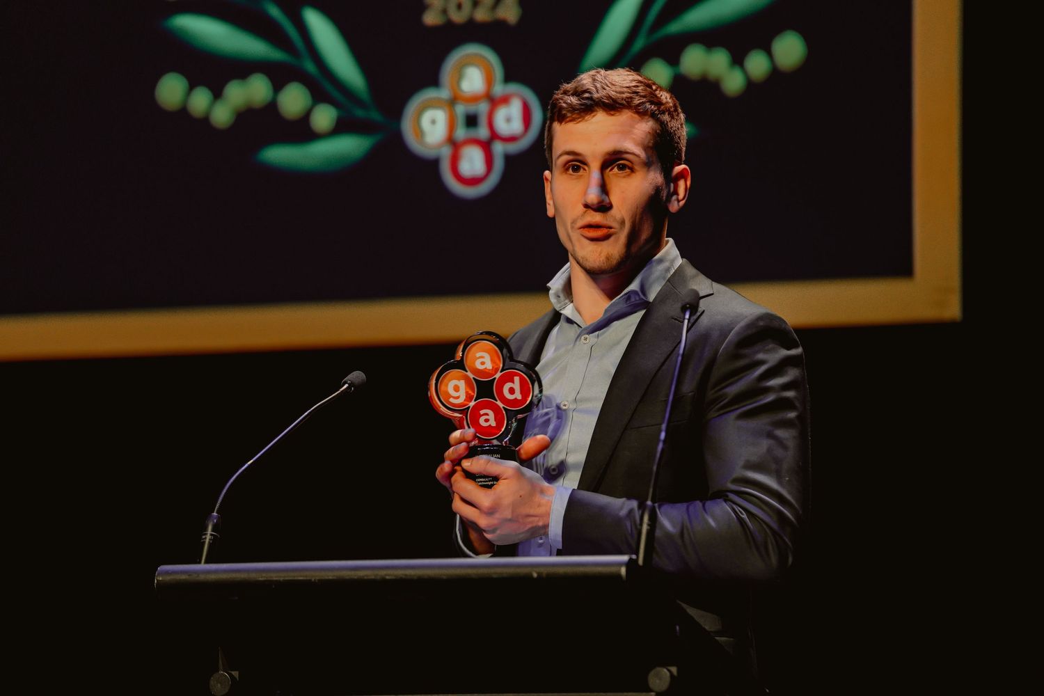A person in a dark suit holds a red toy gun while standing in front of a black background.