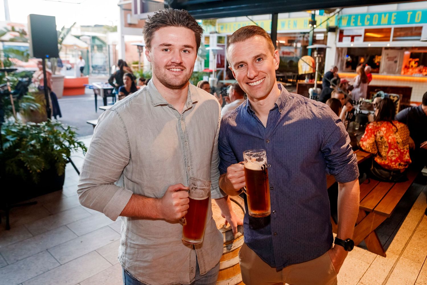 Two people smile and hold beer glasses in what appears to be a social gathering at a bar or restaurant.