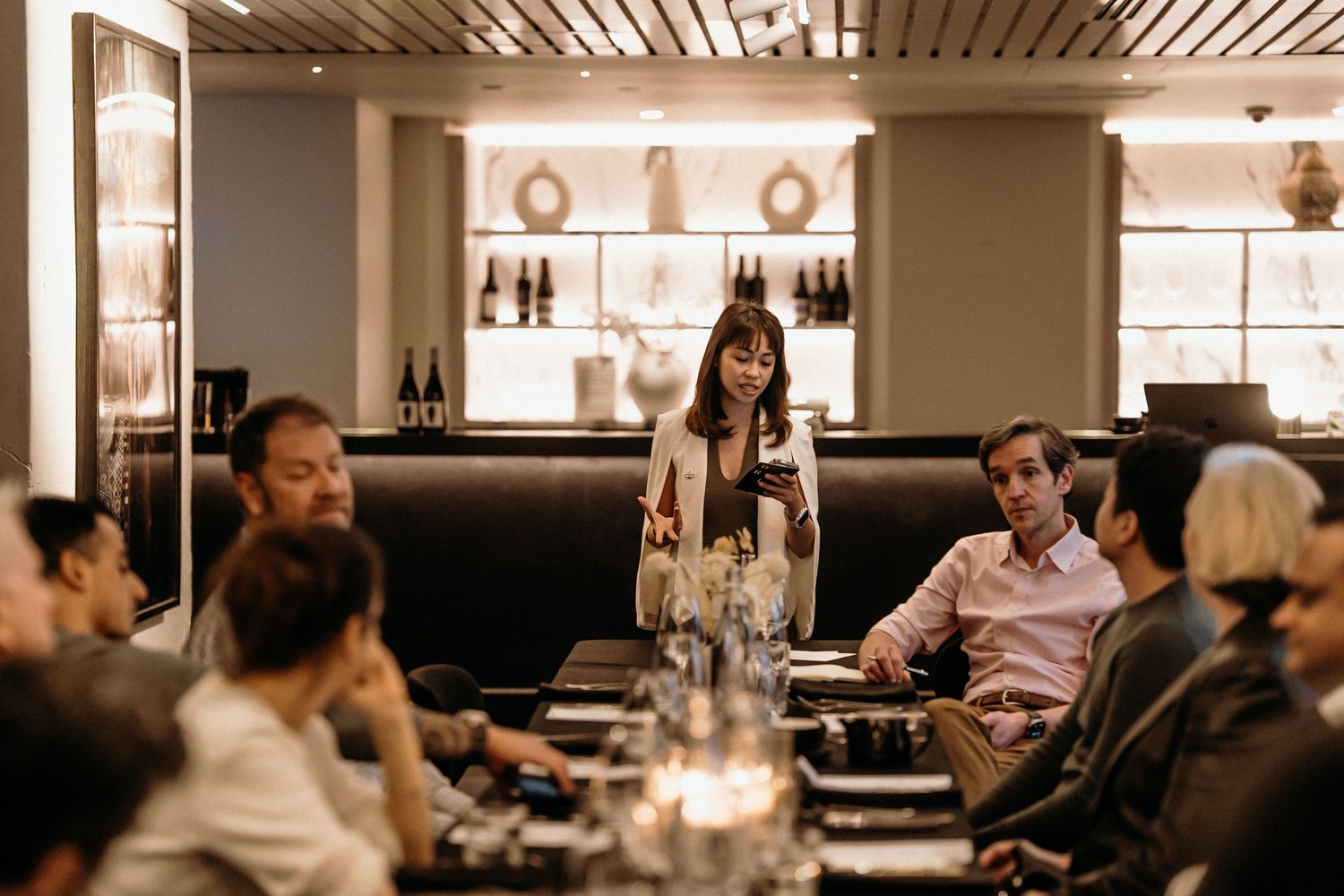 A dimly lit restaurant interior with wooden slat ceiling and people dining at tables in a warm, ambient atmosphere.