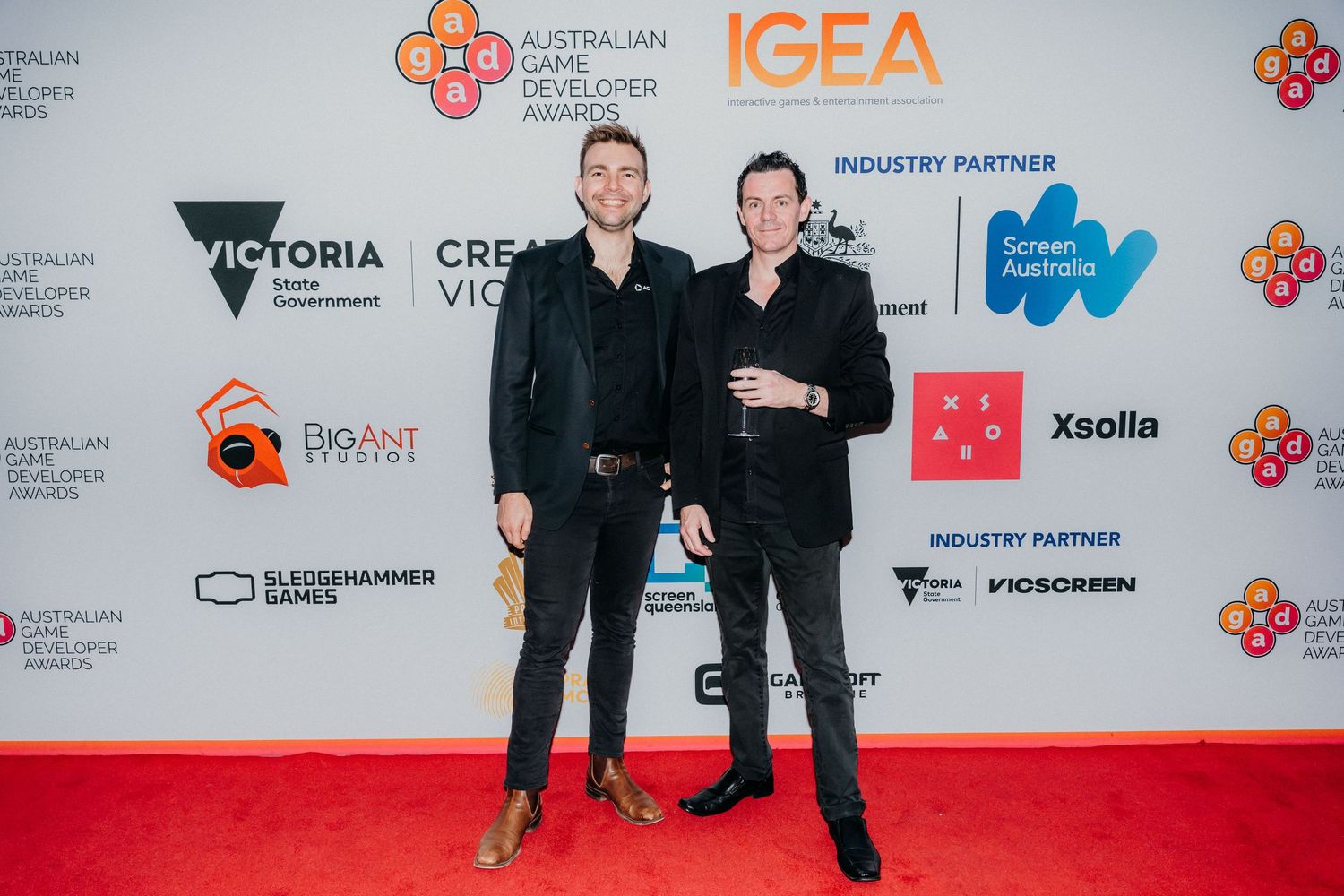 People pose for photos on red carpet at event with sponsor logos and branding wall backdrop.