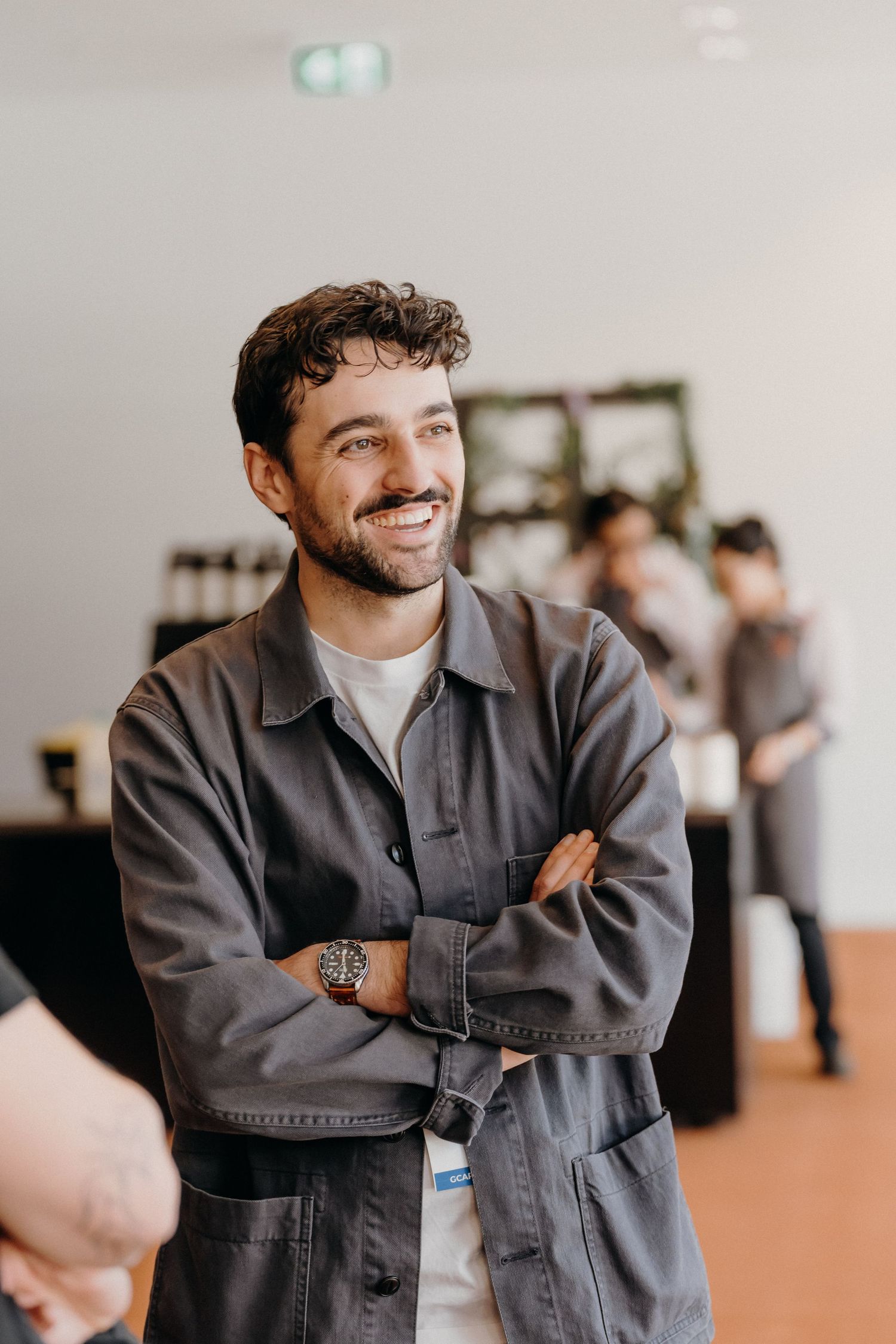Person in a gray jacket smiles and laughs while sitting in a bright indoor space.
