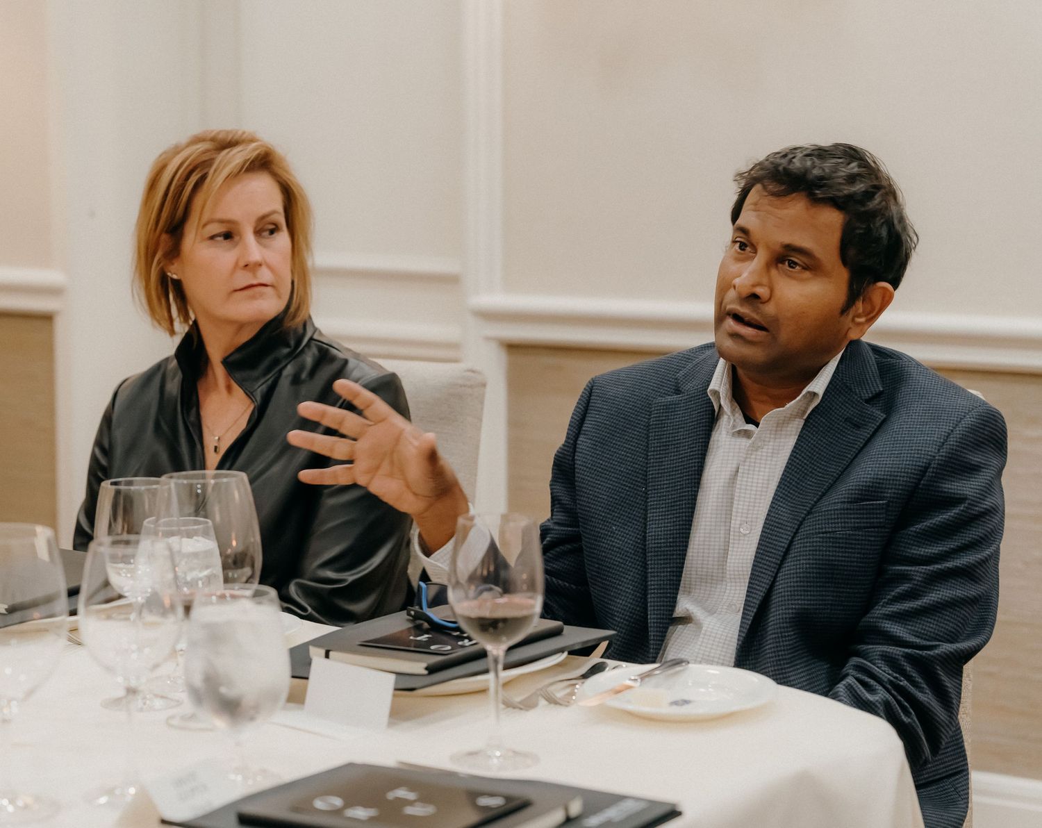 Business professionals sitting at a white table during a meeting or conference with wine glasses and place settings.