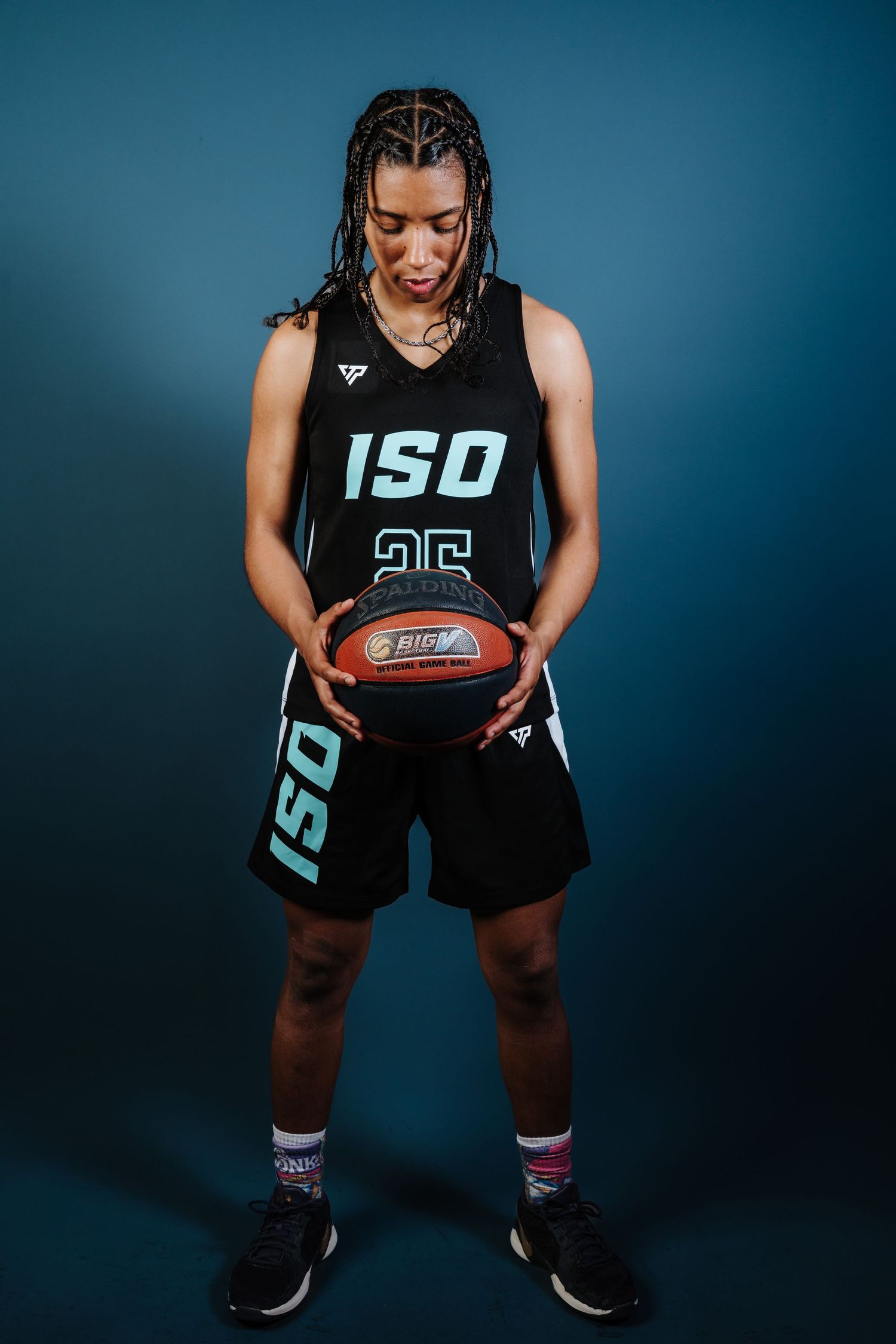 Basketball player in black ISO jersey crouches with ball against dark blue backdrop in dynamic sports photoshoot.