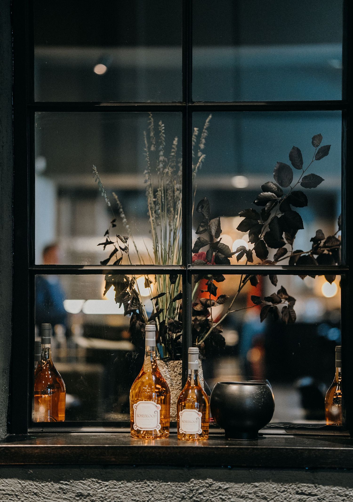 Decorative glass bottles and dried flowers silhouetted in a window display create a moody atmospheric scene.