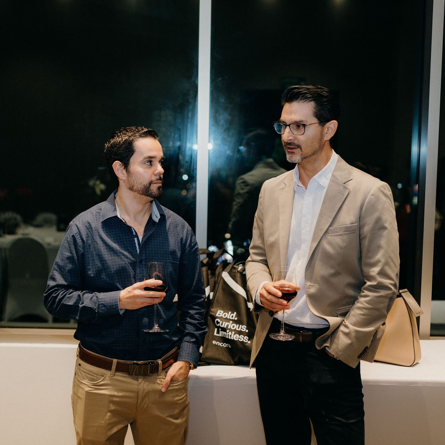 Two colleagues in business attire having an animated conversation in a modern office setting at night.