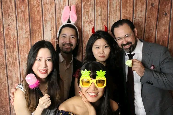 A group of friends poses together with fun party props and accessories against a wooden wall backdrop.