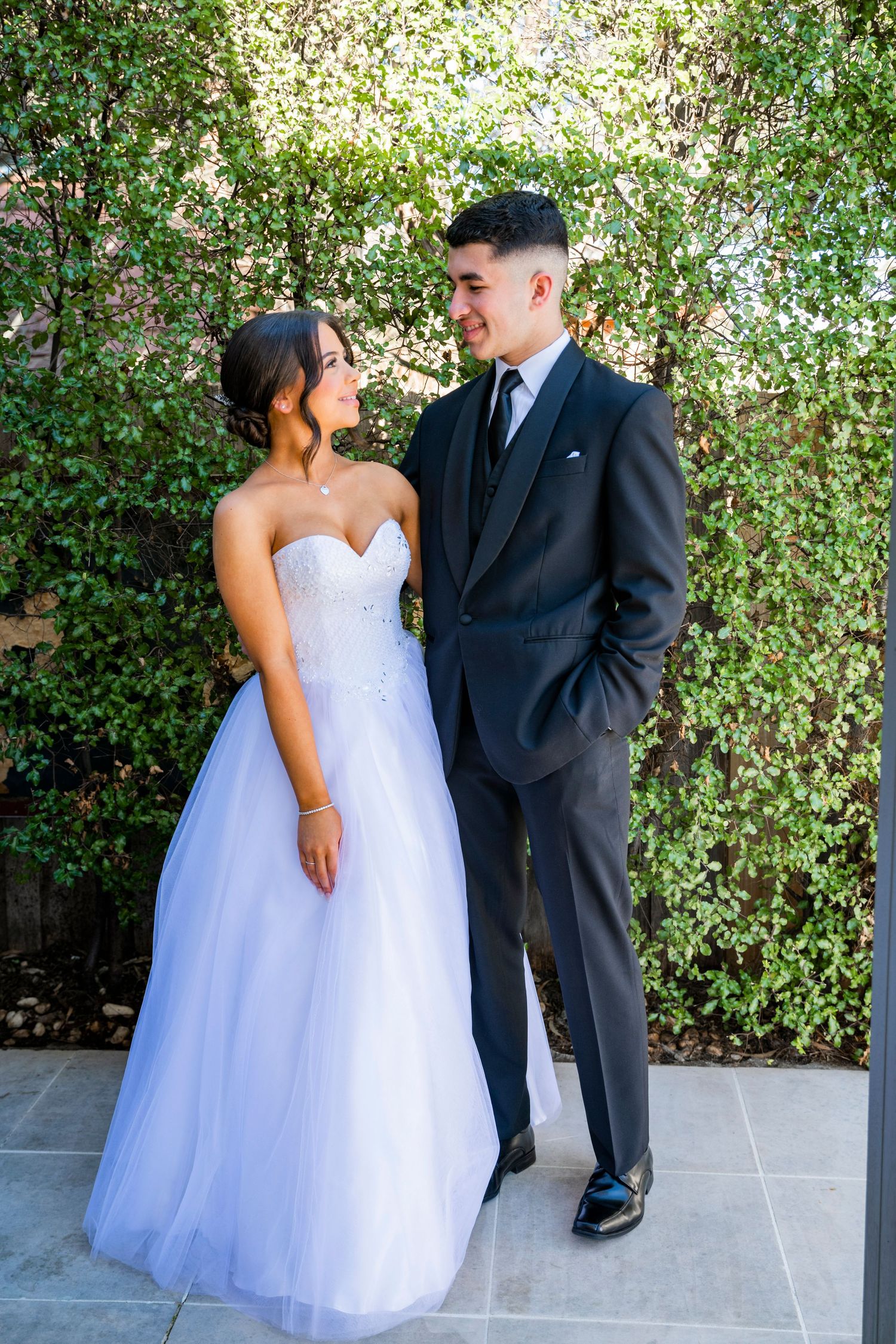 A bride and groom share romantic moments together in a series of photos against a lush green hedge background.
