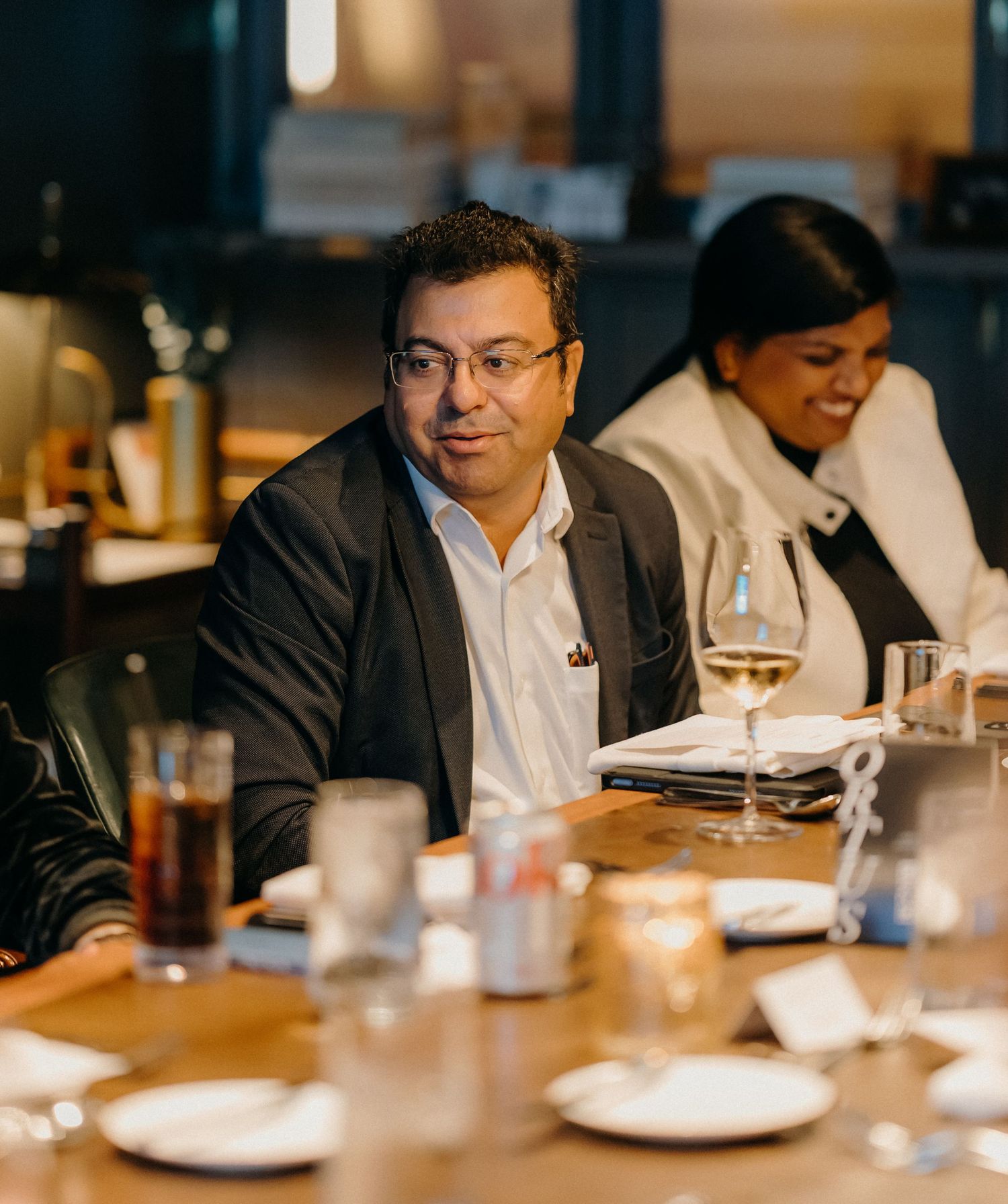 Business professionals dining at a restaurant table with wine glasses and white plates in a dimly lit setting.