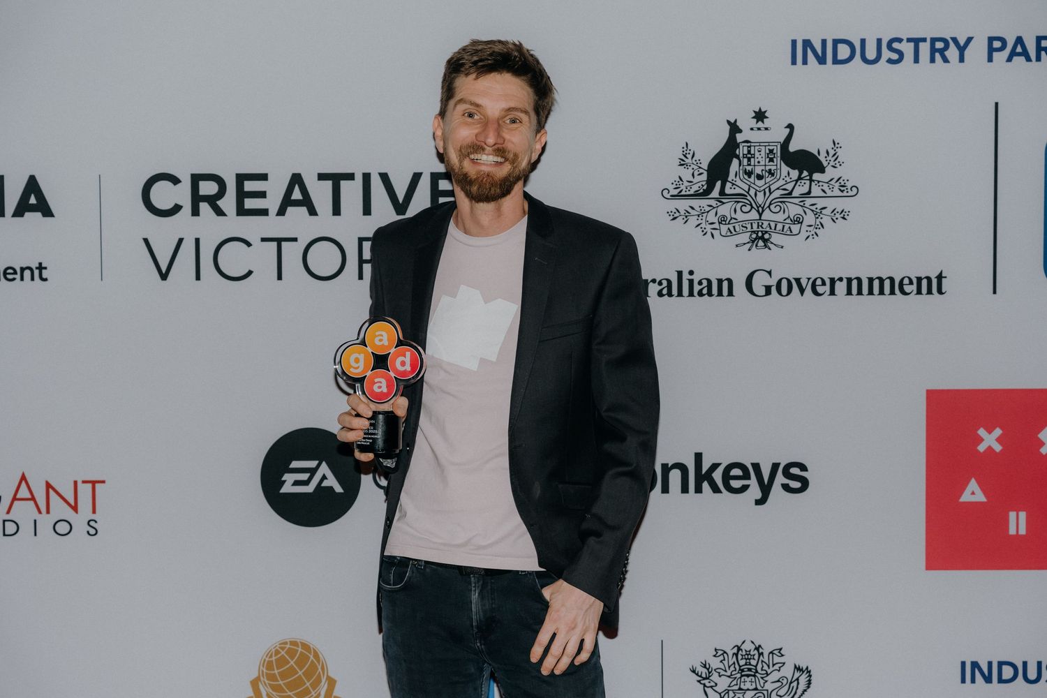 People in formal attire stand against a white backdrop with corporate logos and branding elements visible.