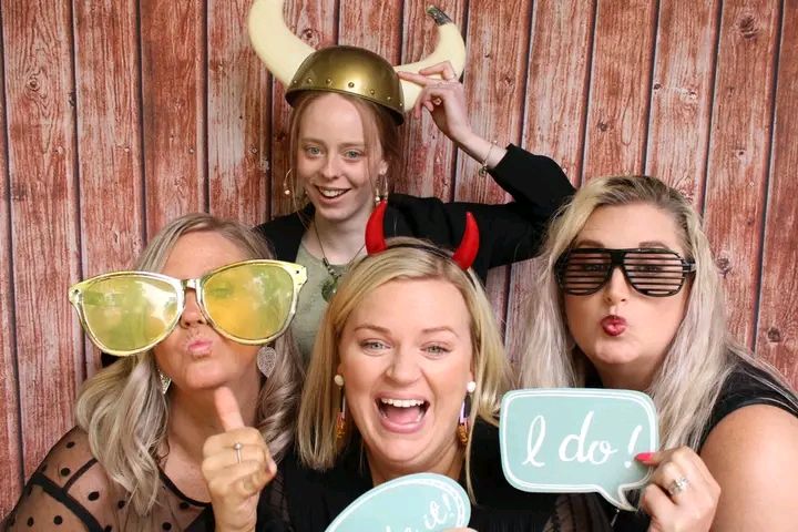 Group of friends posing together with photo booth props against a rustic wooden wall background.