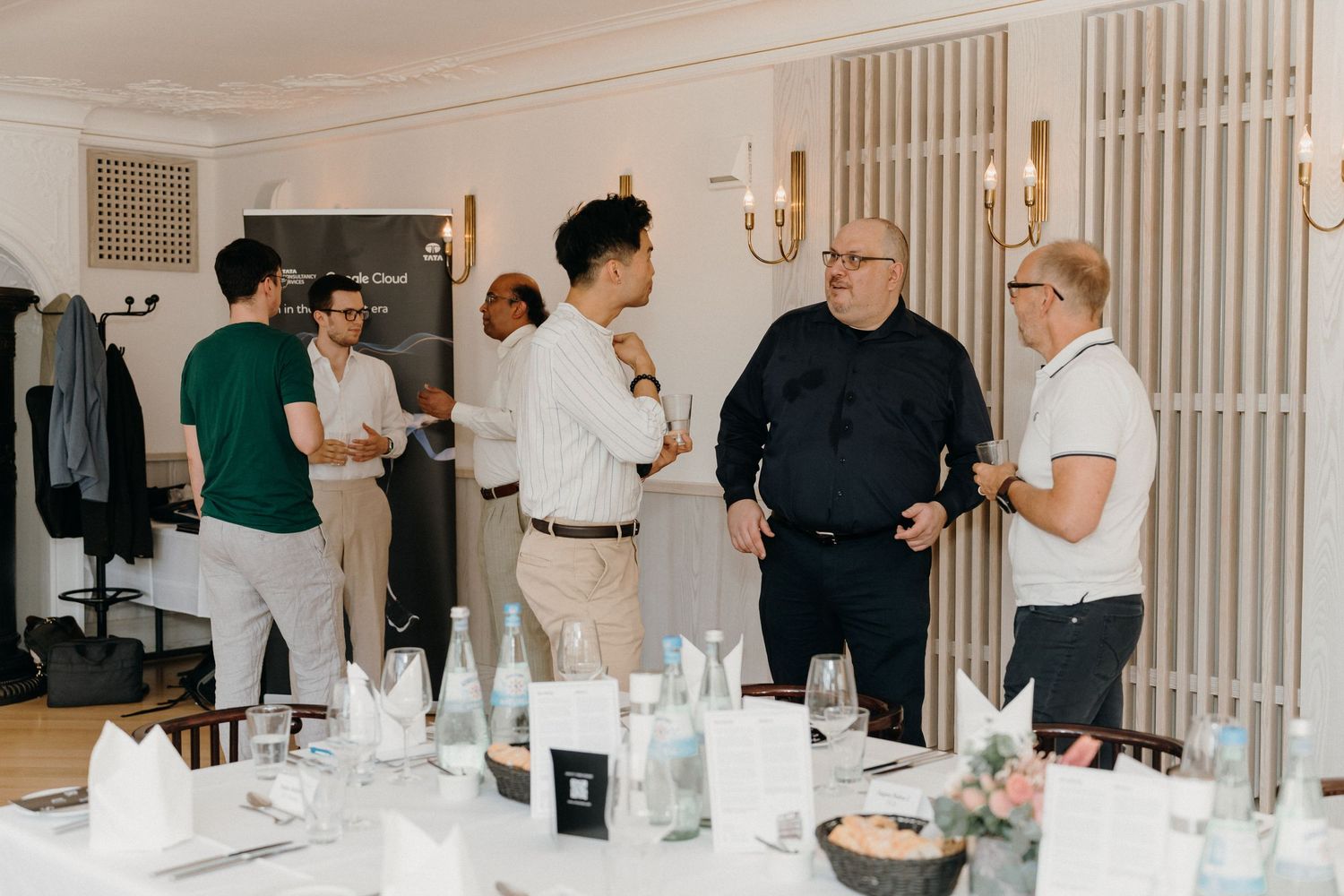 Business professionals networking at an elegant dinner event, standing around a table set with water bottles and glassware.