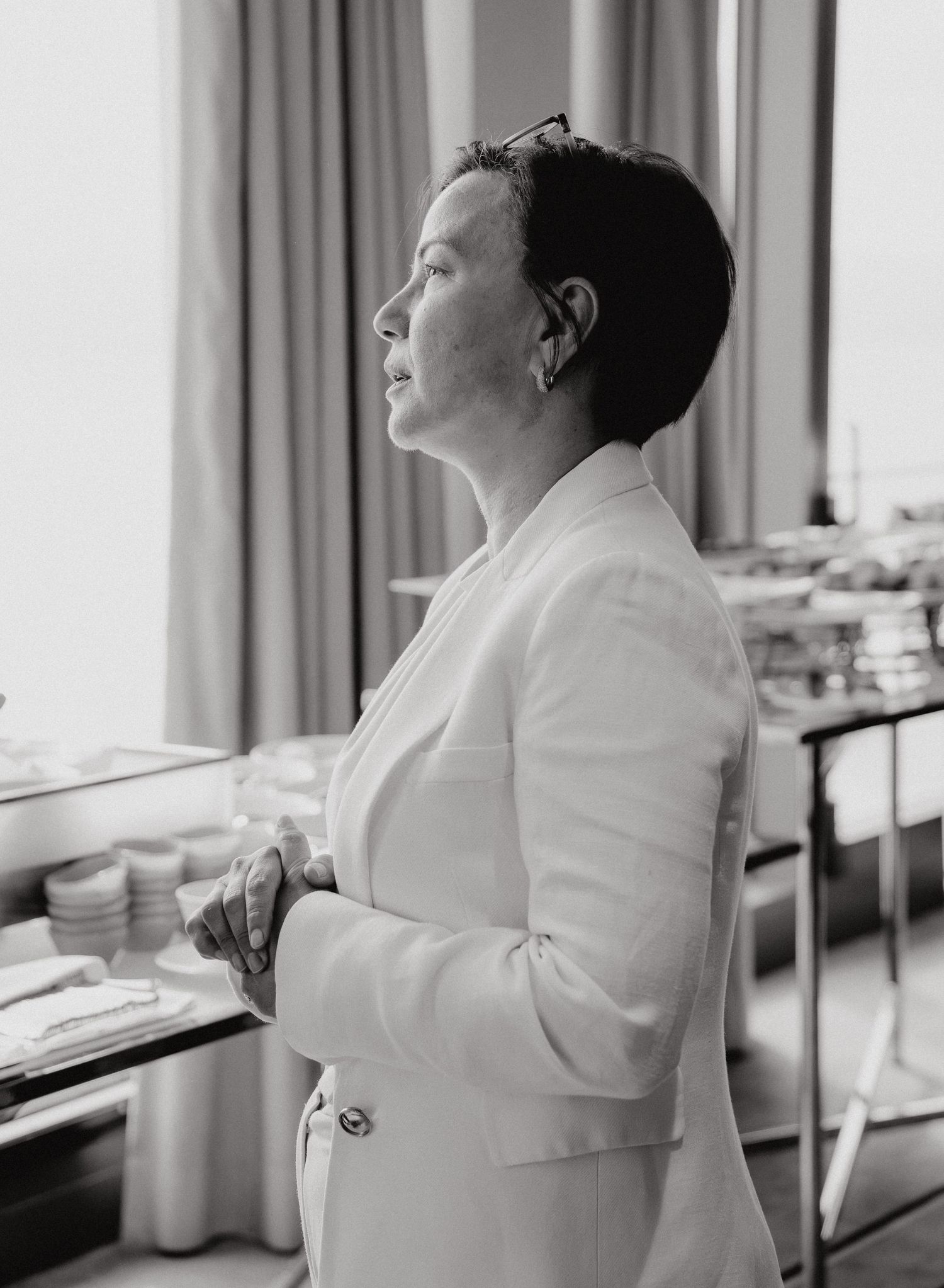 Black and white portrait of a woman in a white blazer with short hair, gazing thoughtfully to the side.