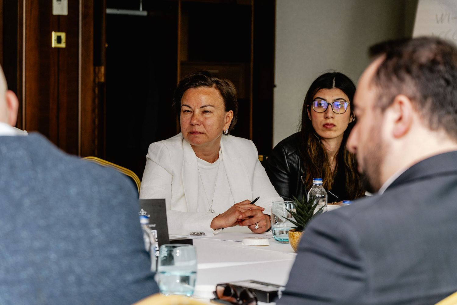 Two businesswomen engaged in discussion at a corporate roundtable meeting in a formal setting.
