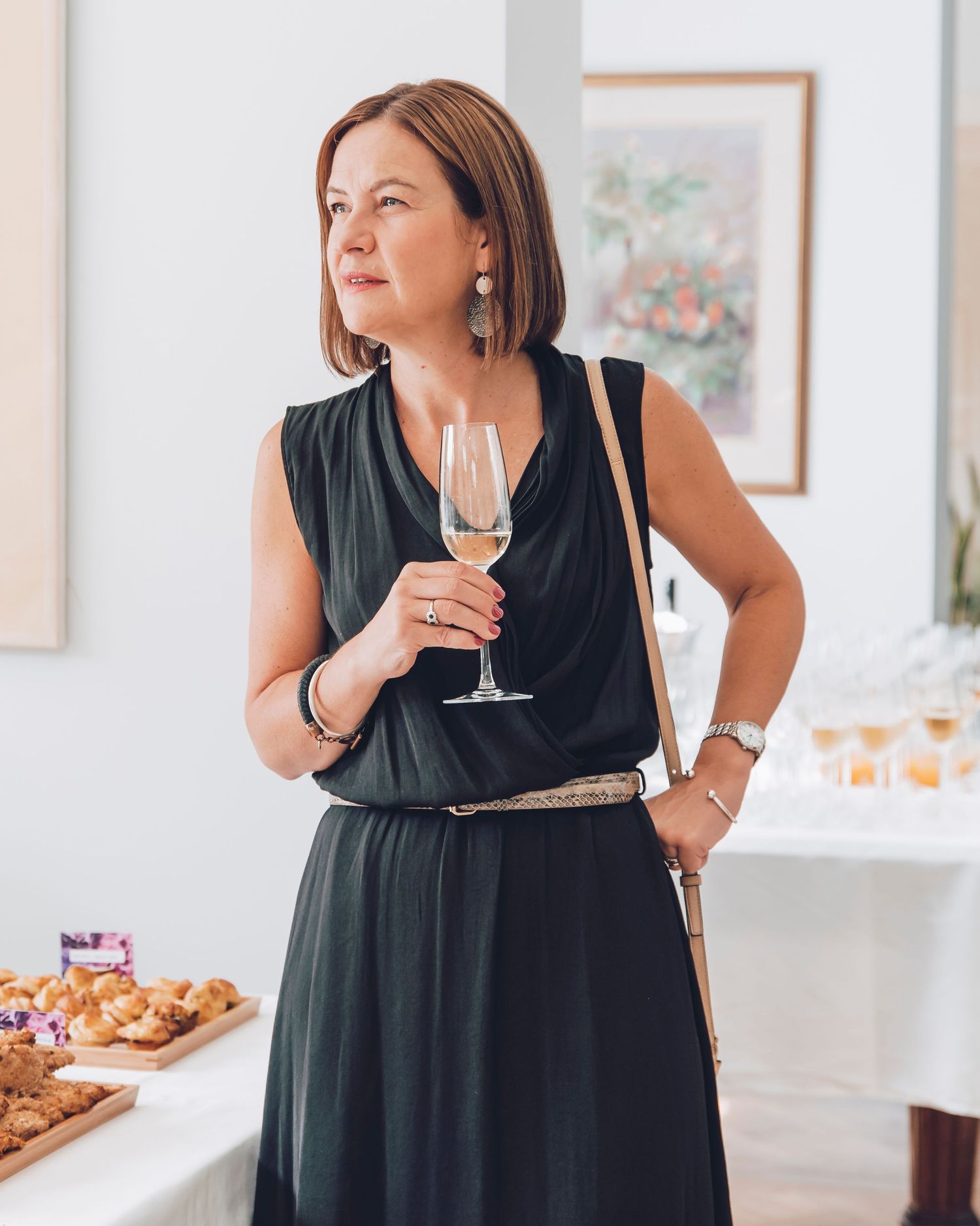 Woman in black dress enjoying wine at a gallery opening.