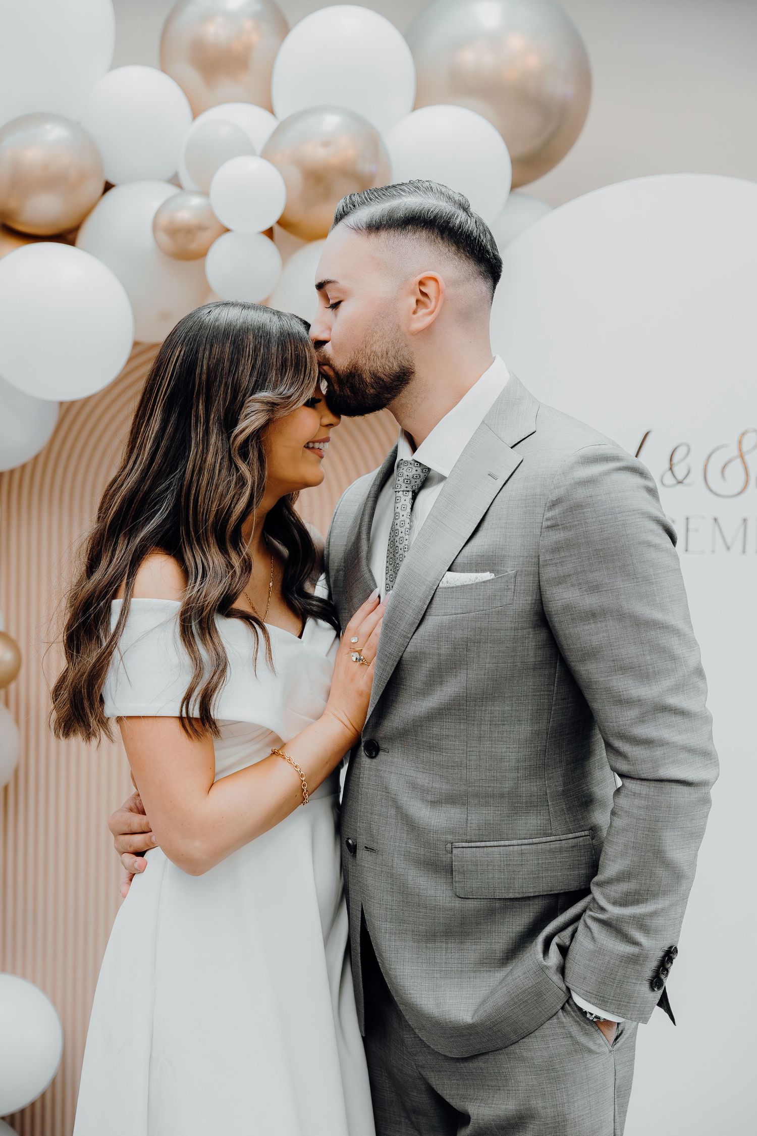 Wedding couple in soft gray and white sharing romantic moments against a backdrop of white balloons.
