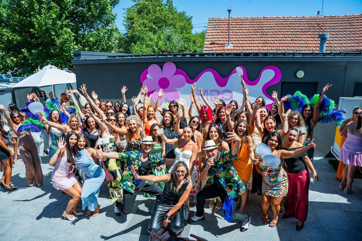 Energetic crowd celebrates at outdoor summer party with colorful wavy decorations and raised hands in joyful atmosphere.