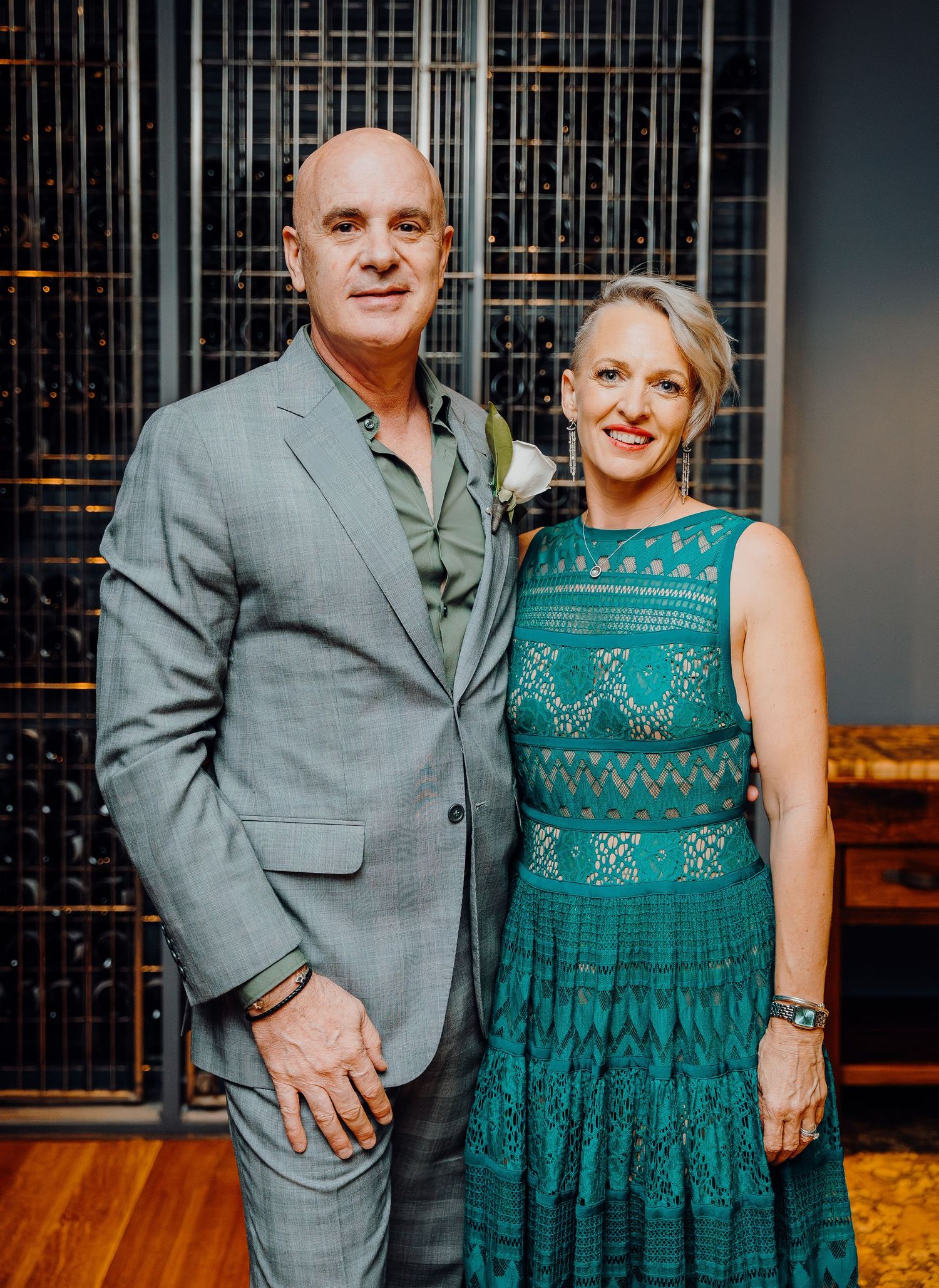 A couple poses together at a wedding venue with industrial decor, showing a grey suit and teal dress combination.