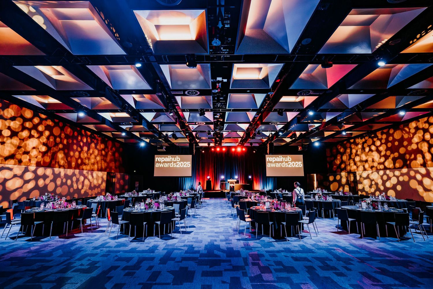 A modern conference venue with colorful lighting and round tables arranged in rows for corporate events.