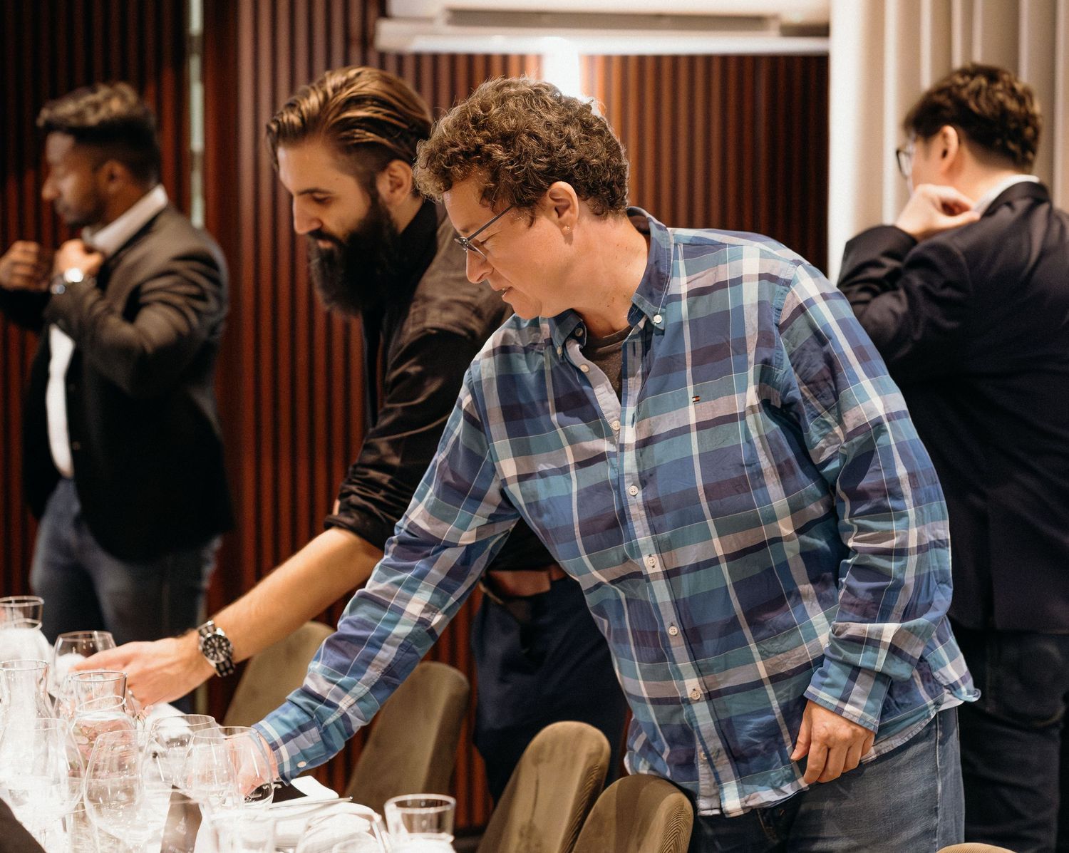 A person in a plaid shirt reaches across a table to arrange items during a setup or preparation event.