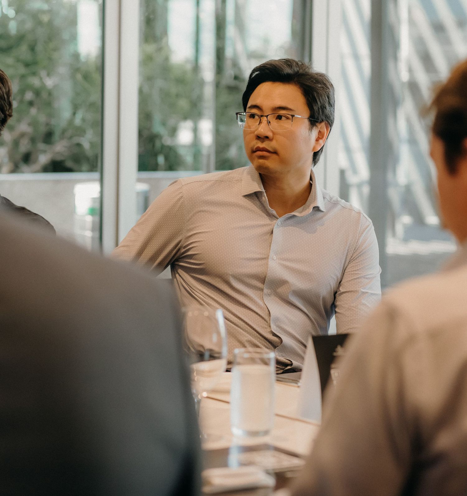Business professional in glasses and light colored shirt listens attentively during meeting in modern office setting.