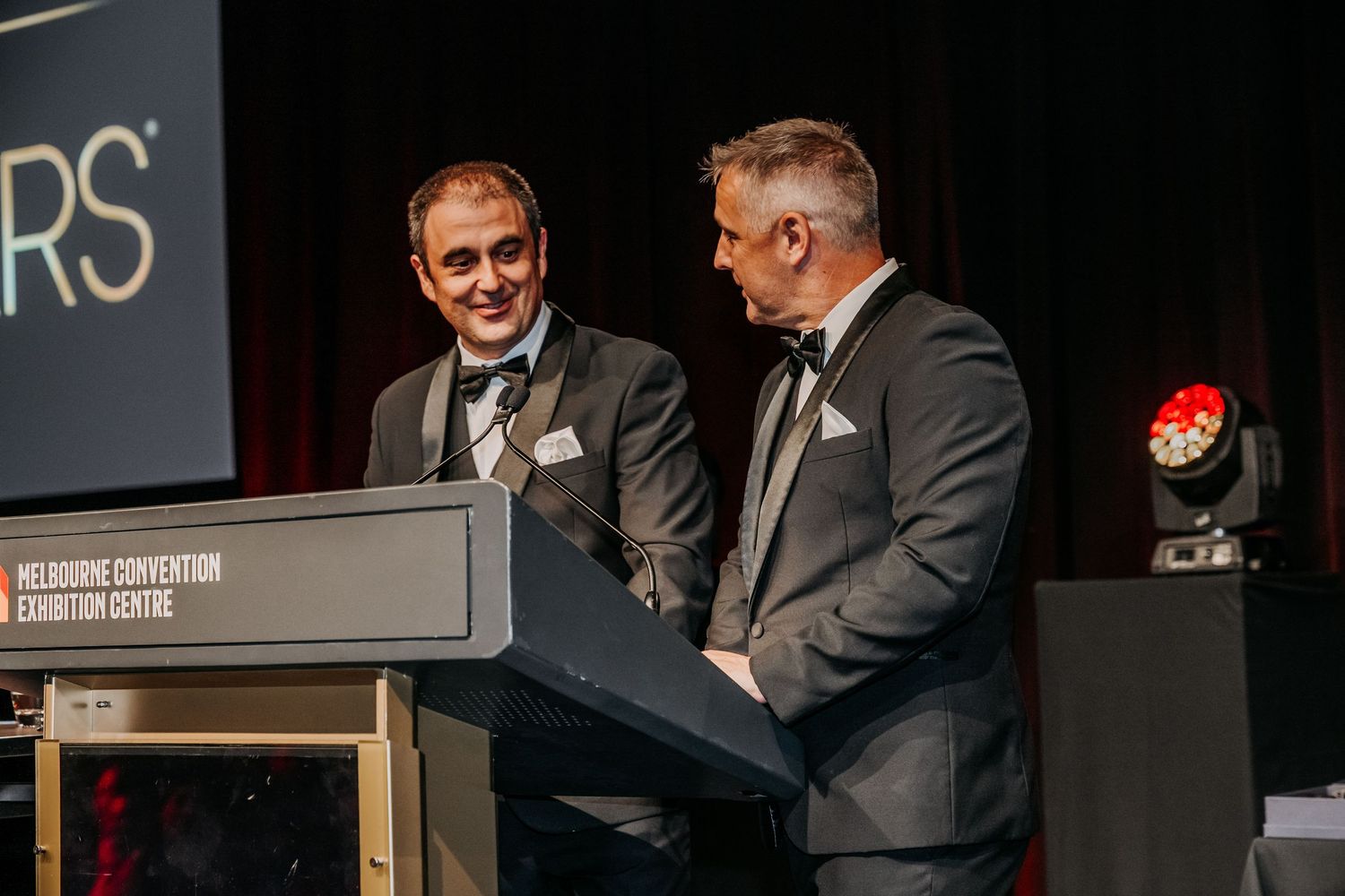 A speaker stands at a podium during a presentation at a professional conference or event.