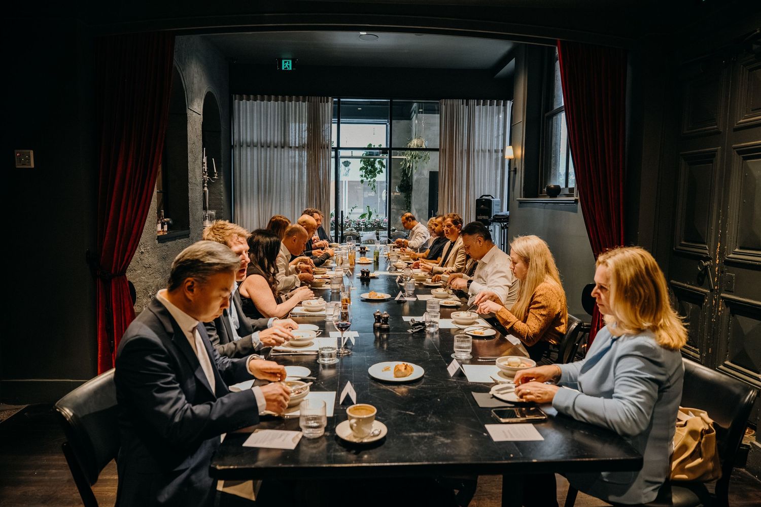 Business professionals gathered around a dark conference table during a meeting in a dimly lit modern office space.