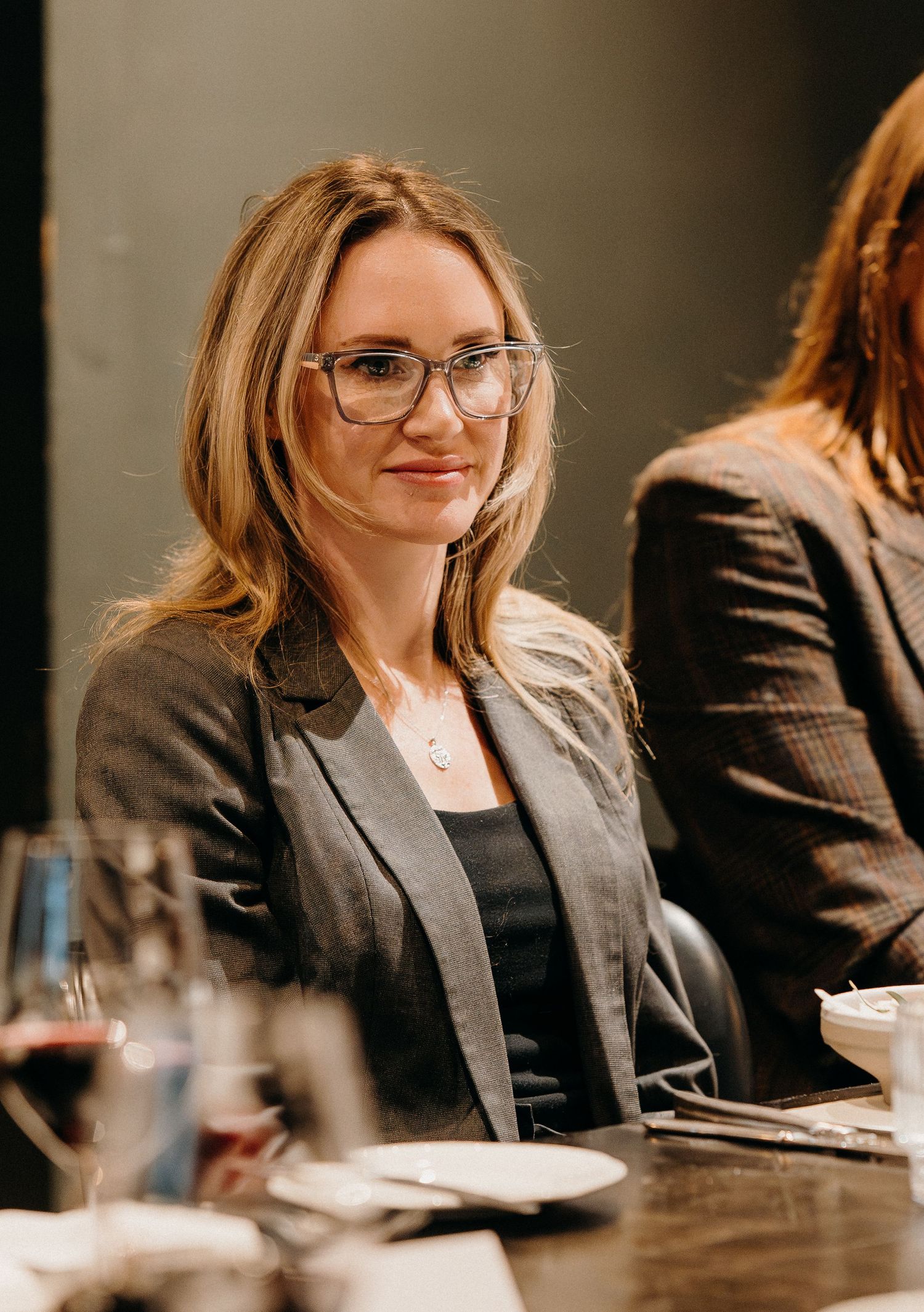 Professional meeting scene showing a person in business attire with glasses seated at a conference table.