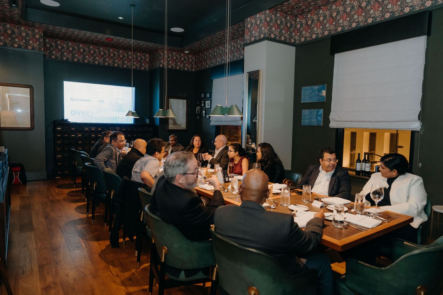 Business professionals seated at long conference tables during a corporate meeting in a modern office space.
