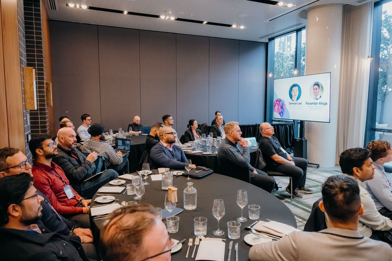 Business professionals attend a corporate conference in a modern meeting room with glass walls and presentation screens.
