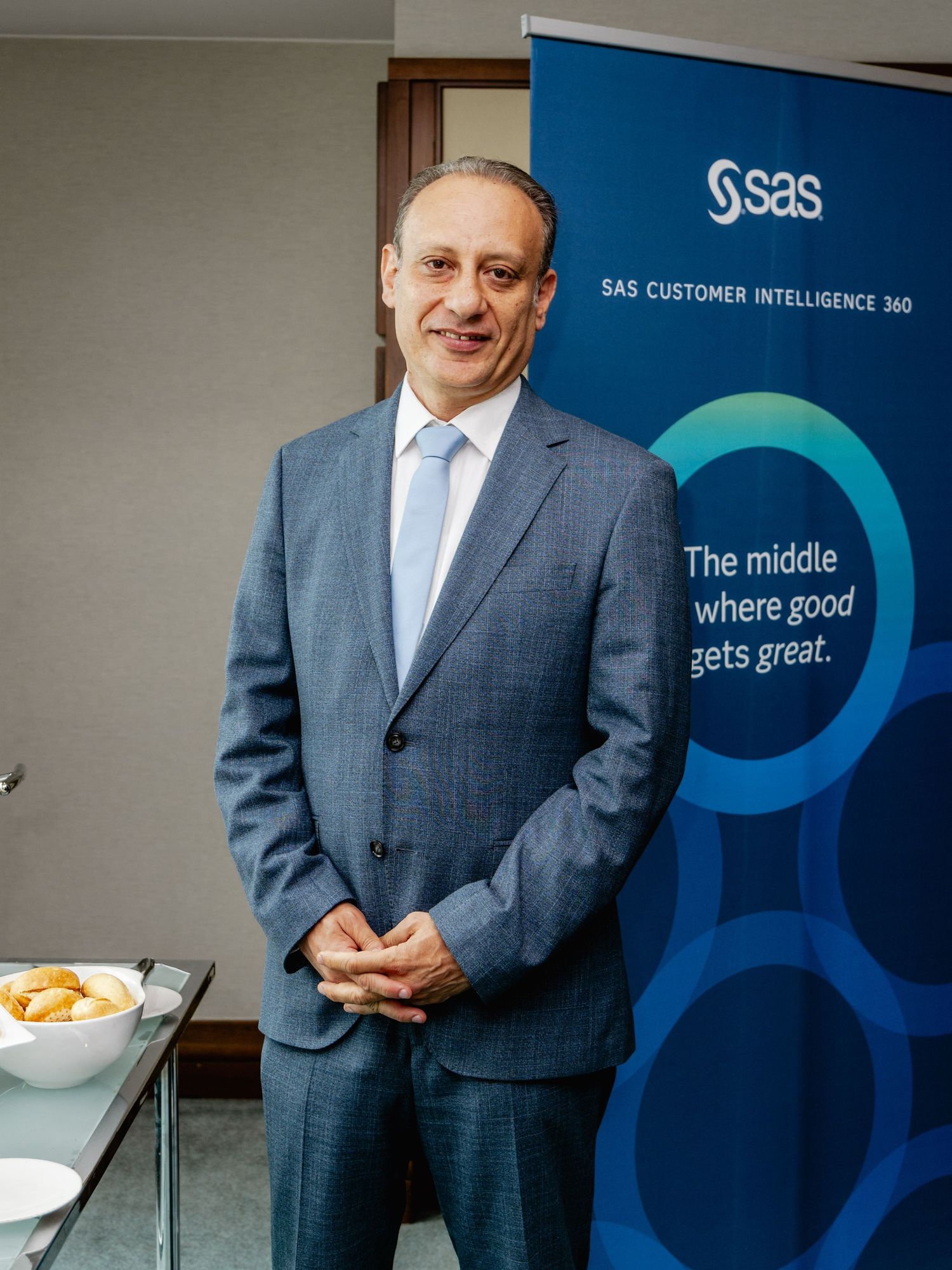 Professional man in blue suit standing beside SAS Customer Intelligence 360 banner at corporate event.