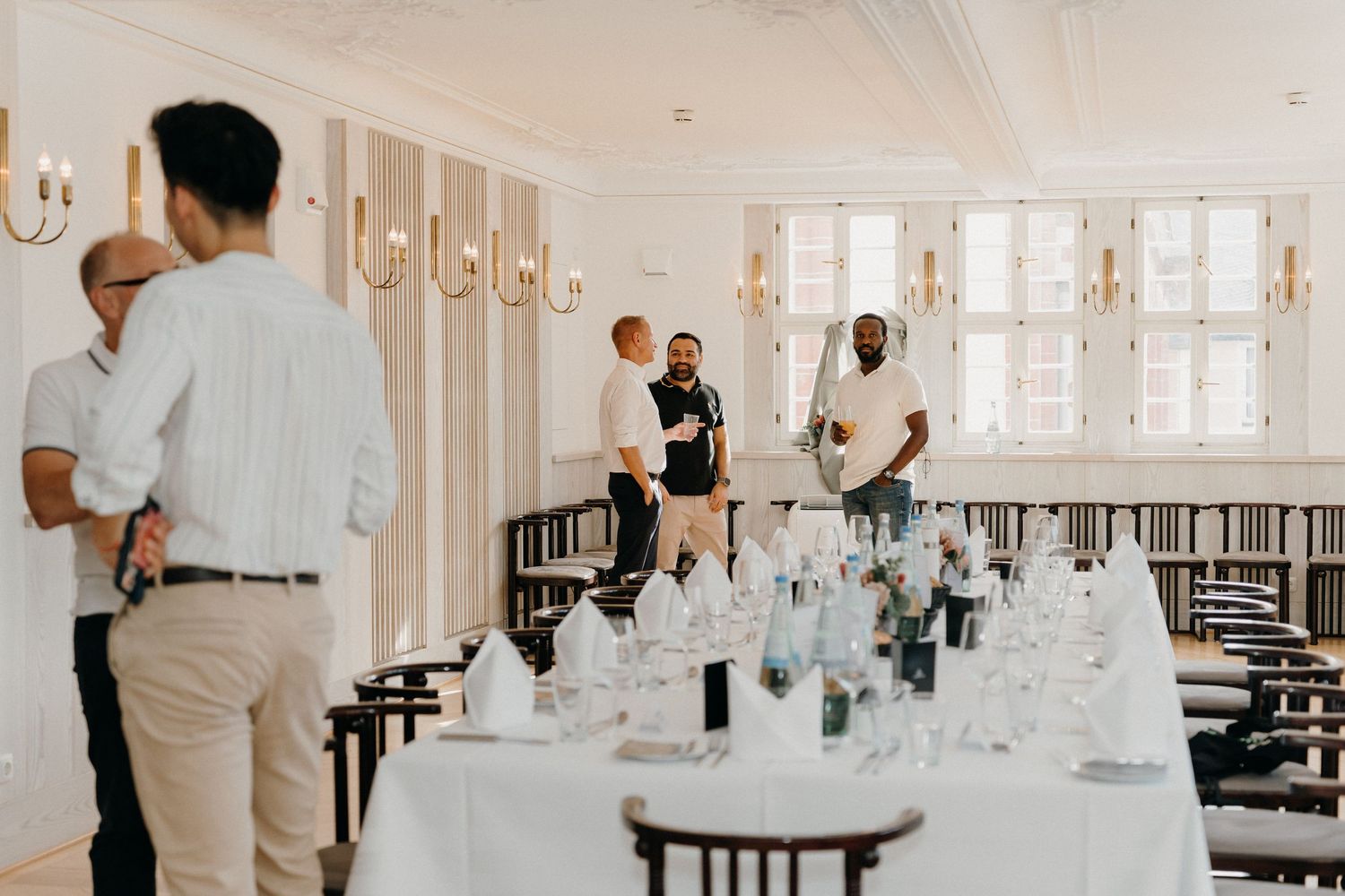 Elegantly set dining room with white tablecloths, glassware, and staff preparing for a formal event.
