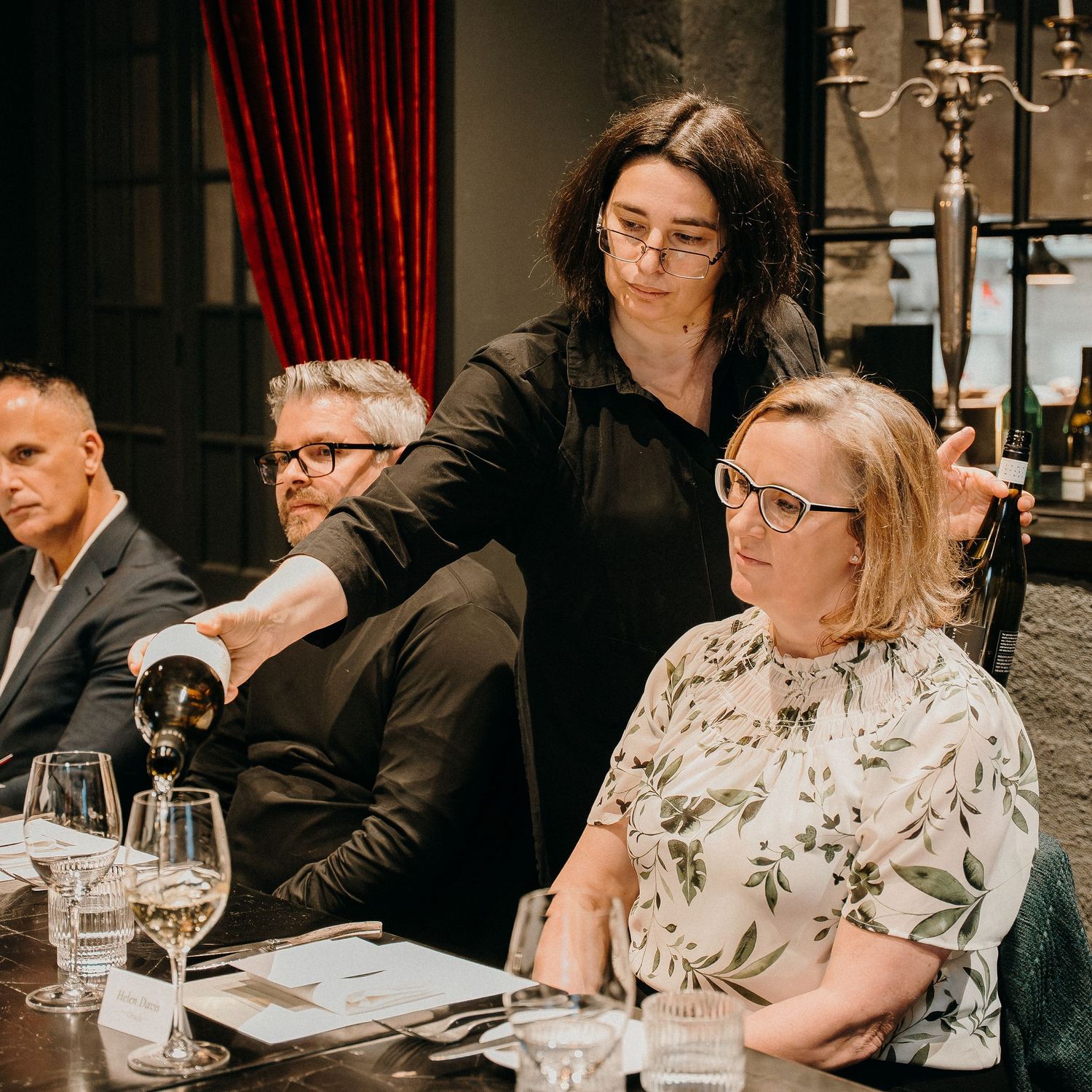 People dining at an upscale restaurant with wine glasses and elegant table settings in a dimly lit atmosphere.