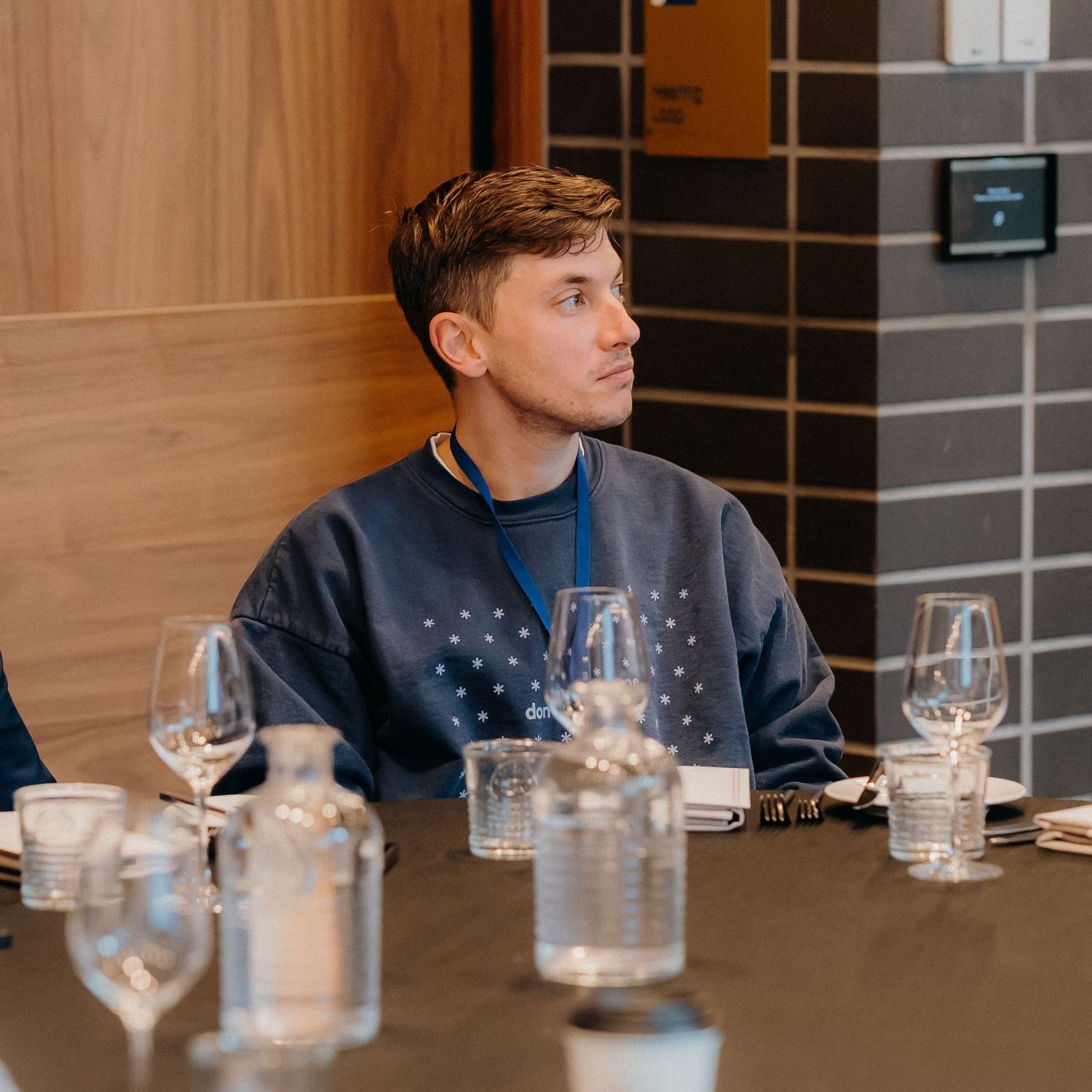 Person sitting at dining table with wine glasses and water glasses in modern restaurant setting.