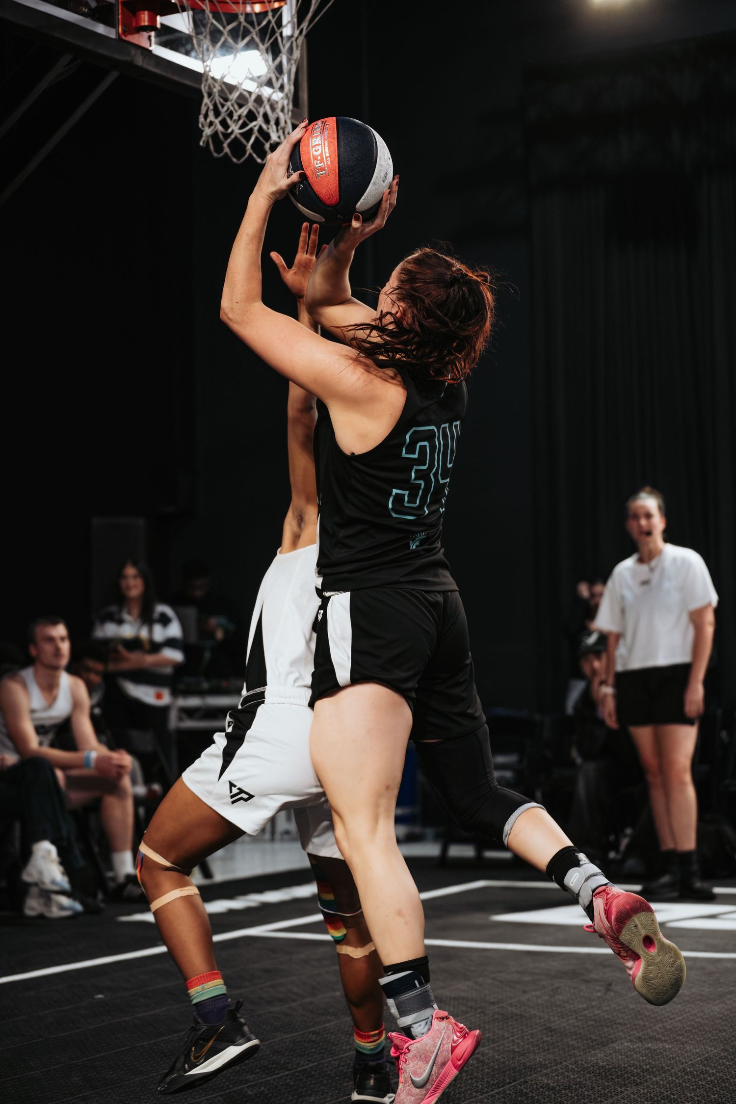 Basketball players compete in an intense game on an indoor court with one player going up for a layup.