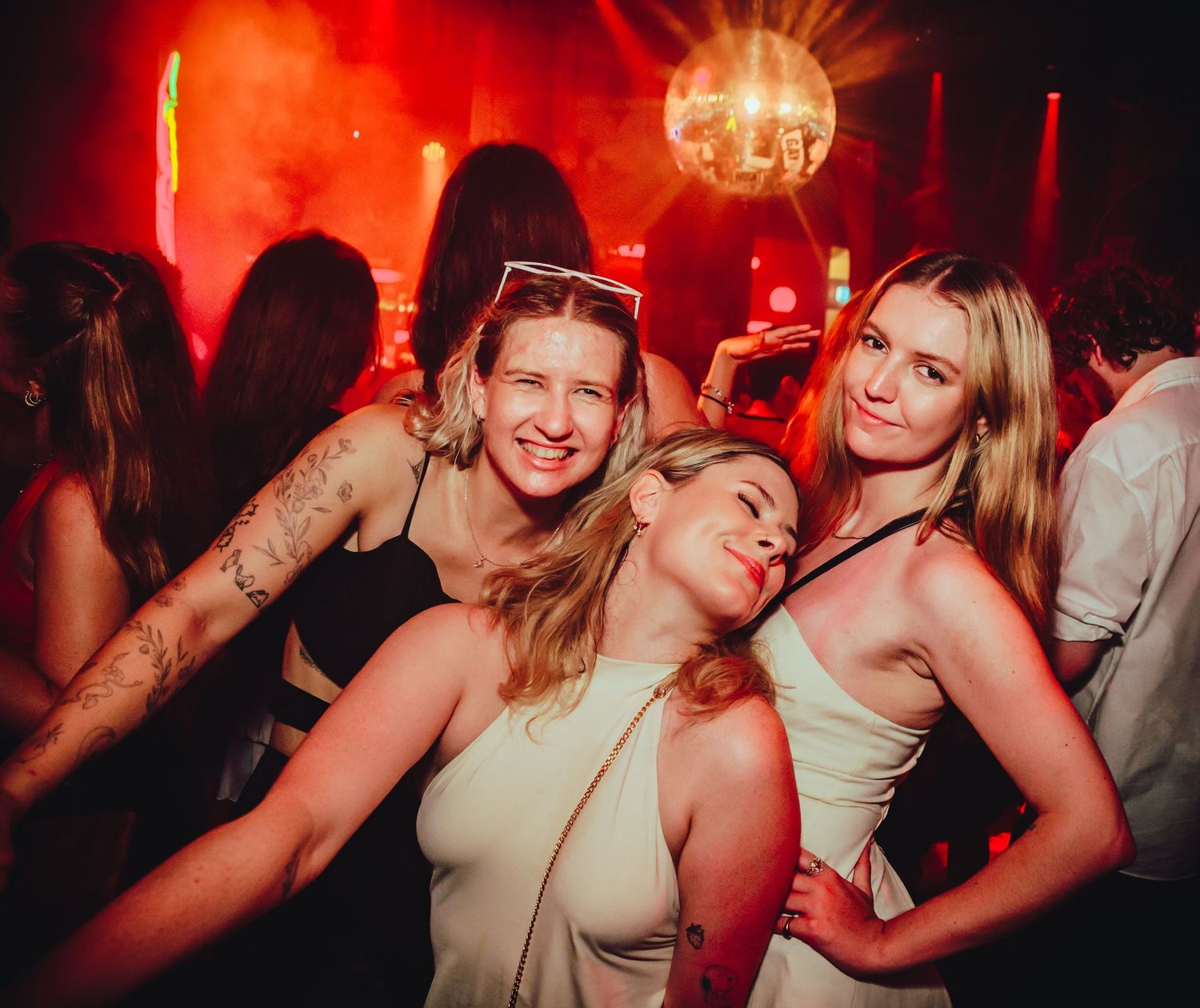 People dancing and socializing together in dimly lit nightclub with red lighting and disco ball atmosphere.