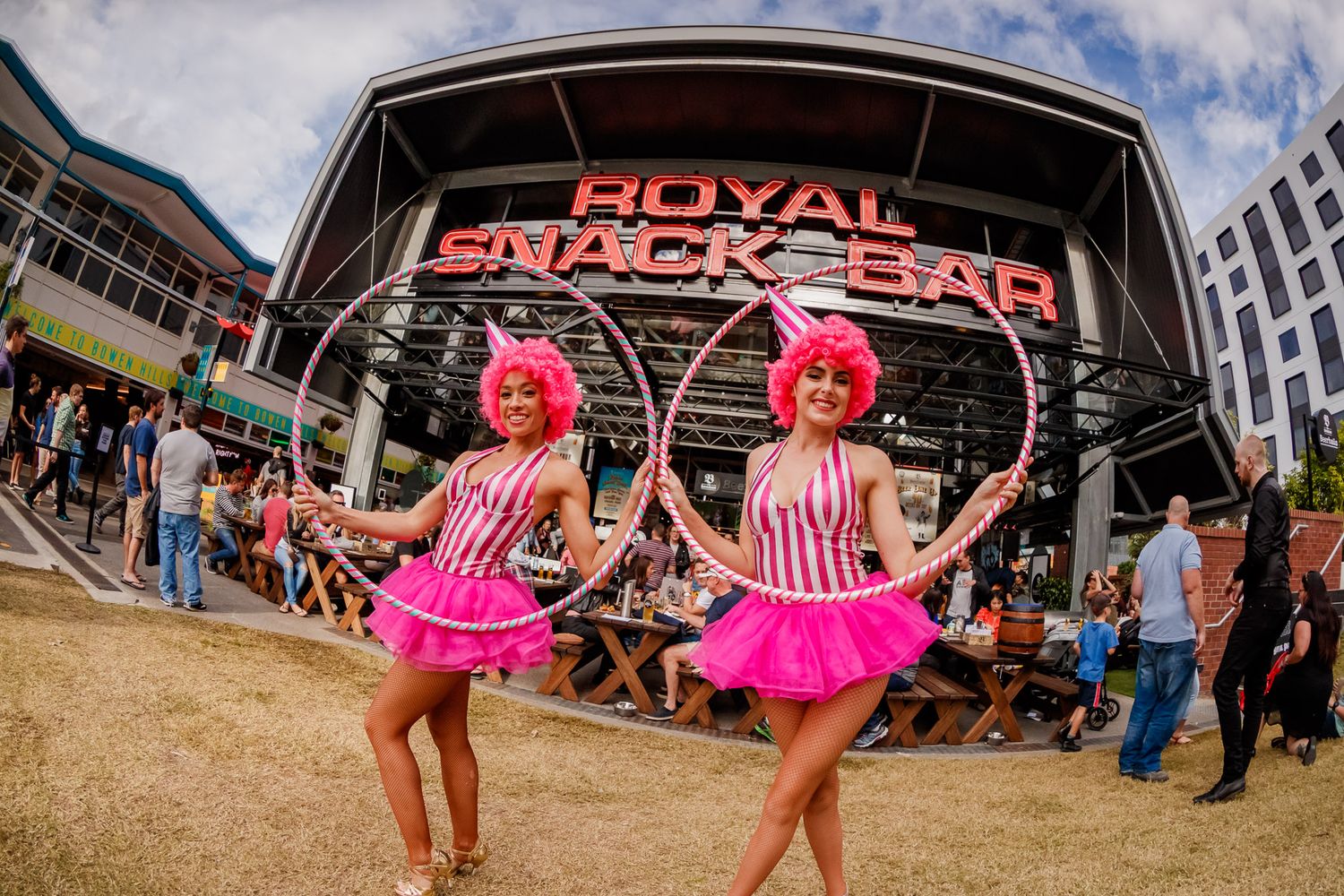 Two performers in pink and white striped outfits with tutus dance with hula hoops in front of the Royal Black Pearl venue.