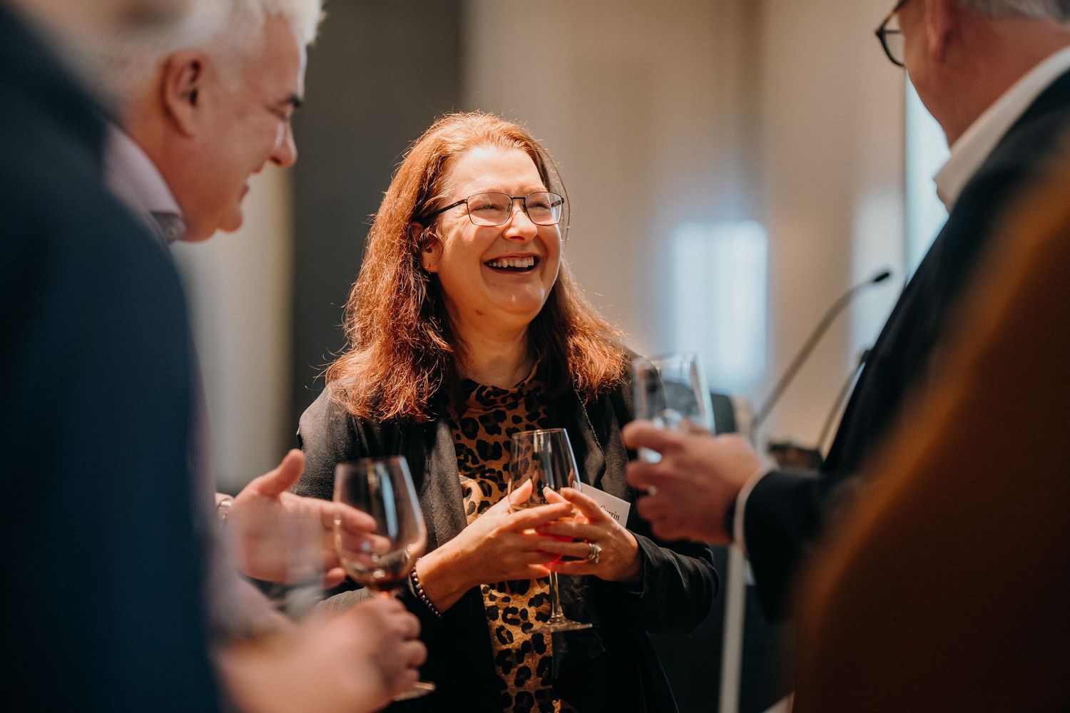 People enjoying conversation and drinks at an elegant social gathering in a bright indoor venue.
