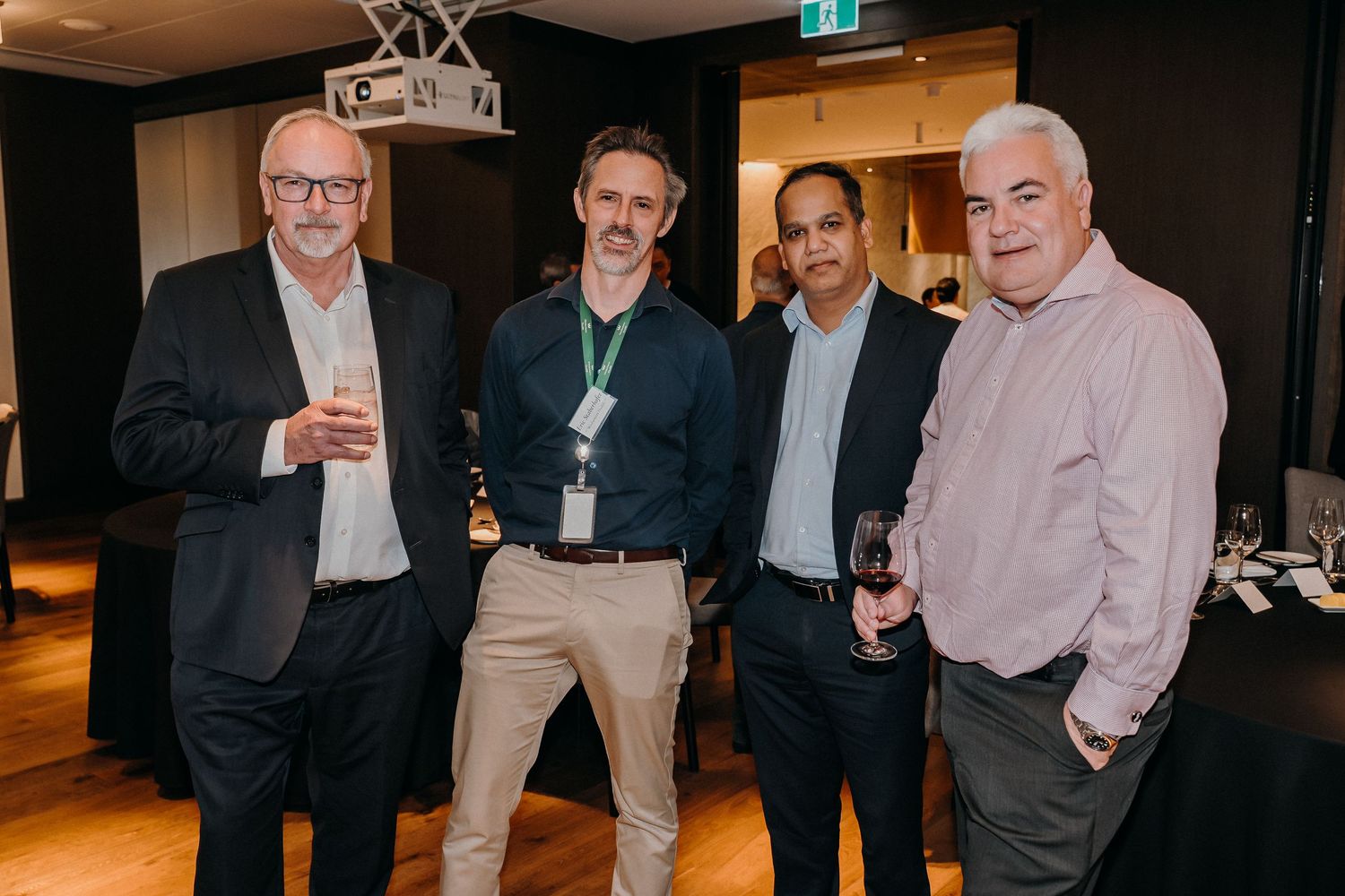 A group of business professionals gather together at a dimly lit indoor event space.