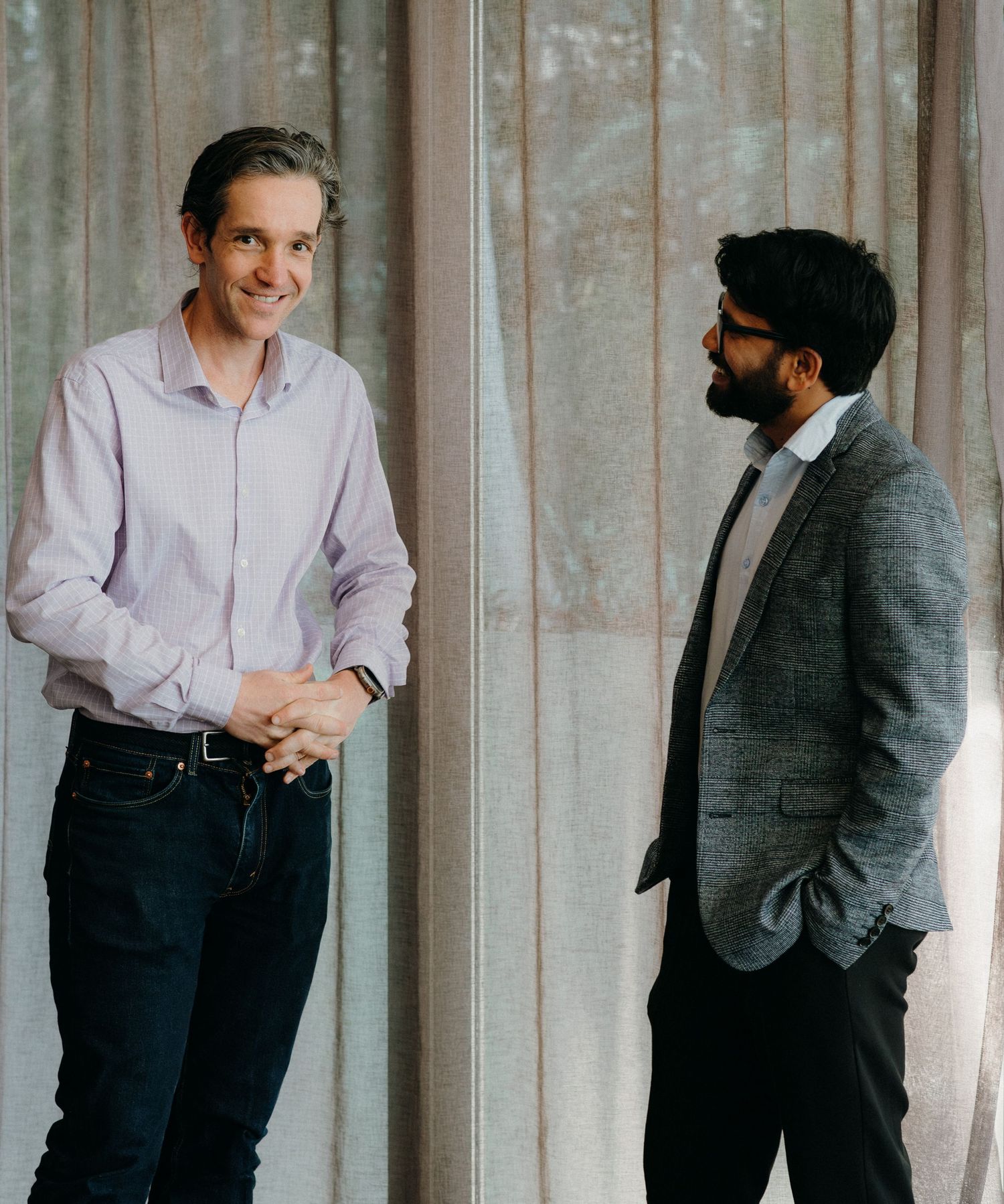 Business professionals in suits and formal attire stand casually against a textured wall in a modern office setting.